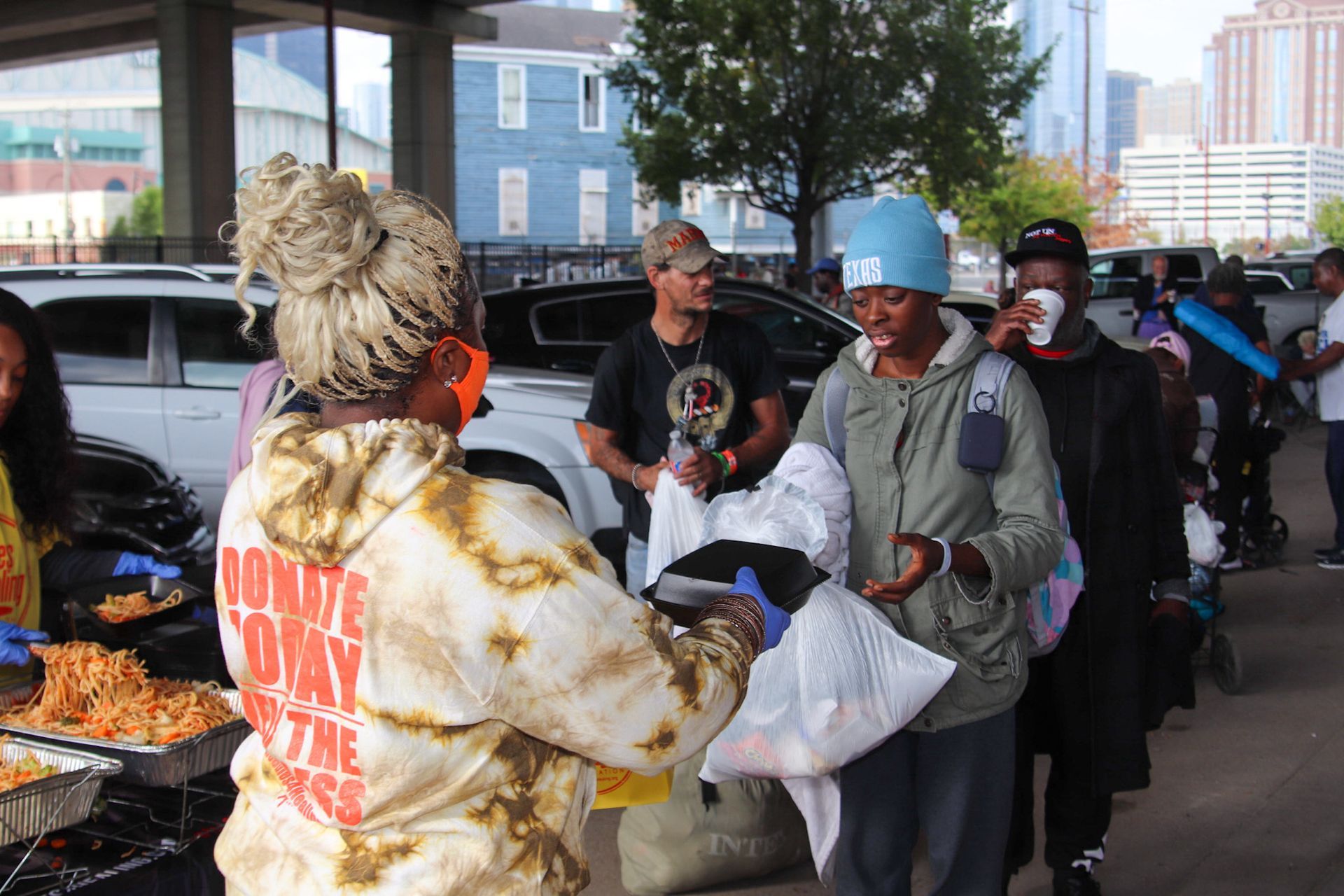 A woman in a tie dye hoodie is serving food to a group of people.
