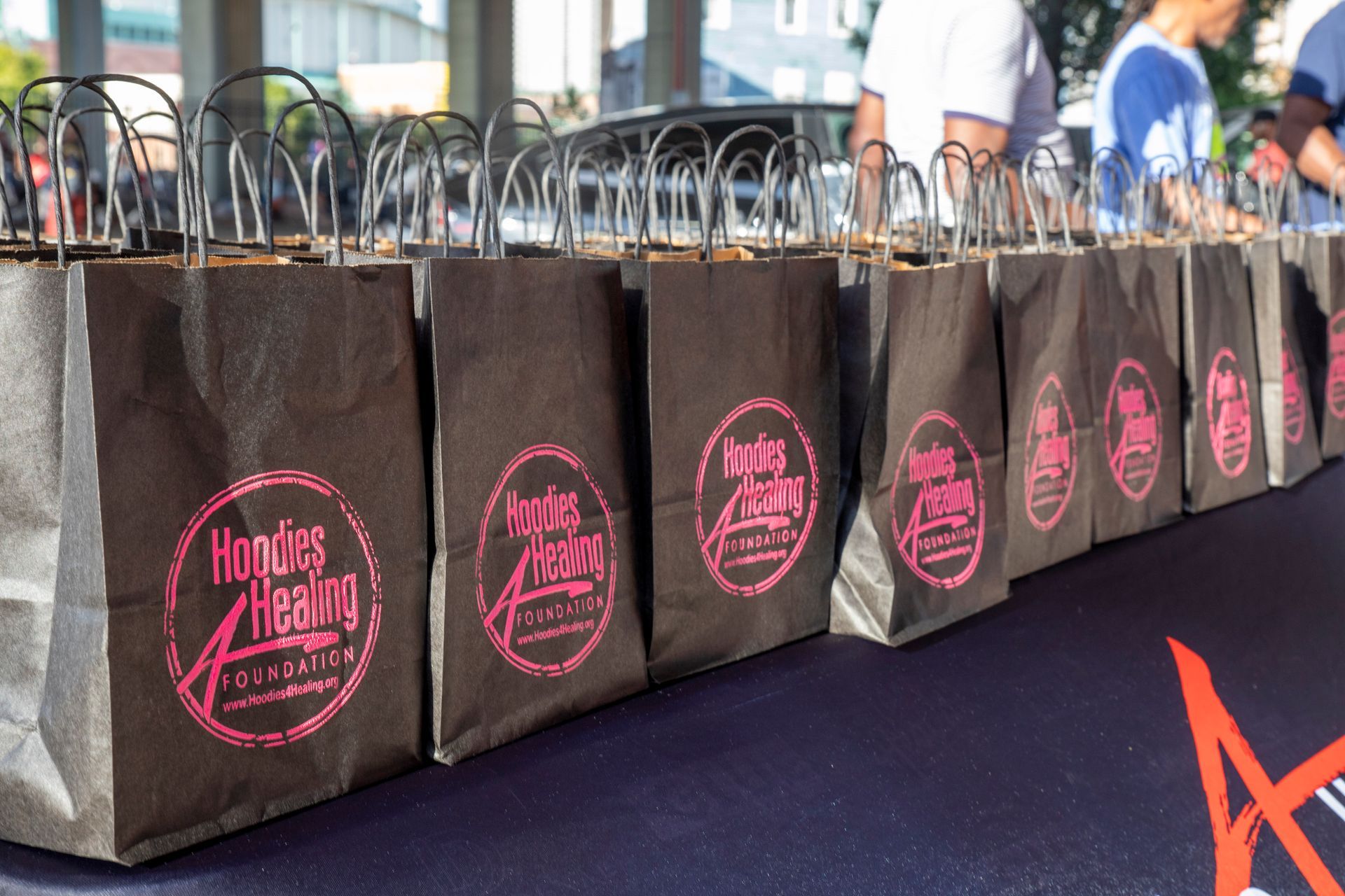 A row of black bags with pink logos on them are lined up on a table.