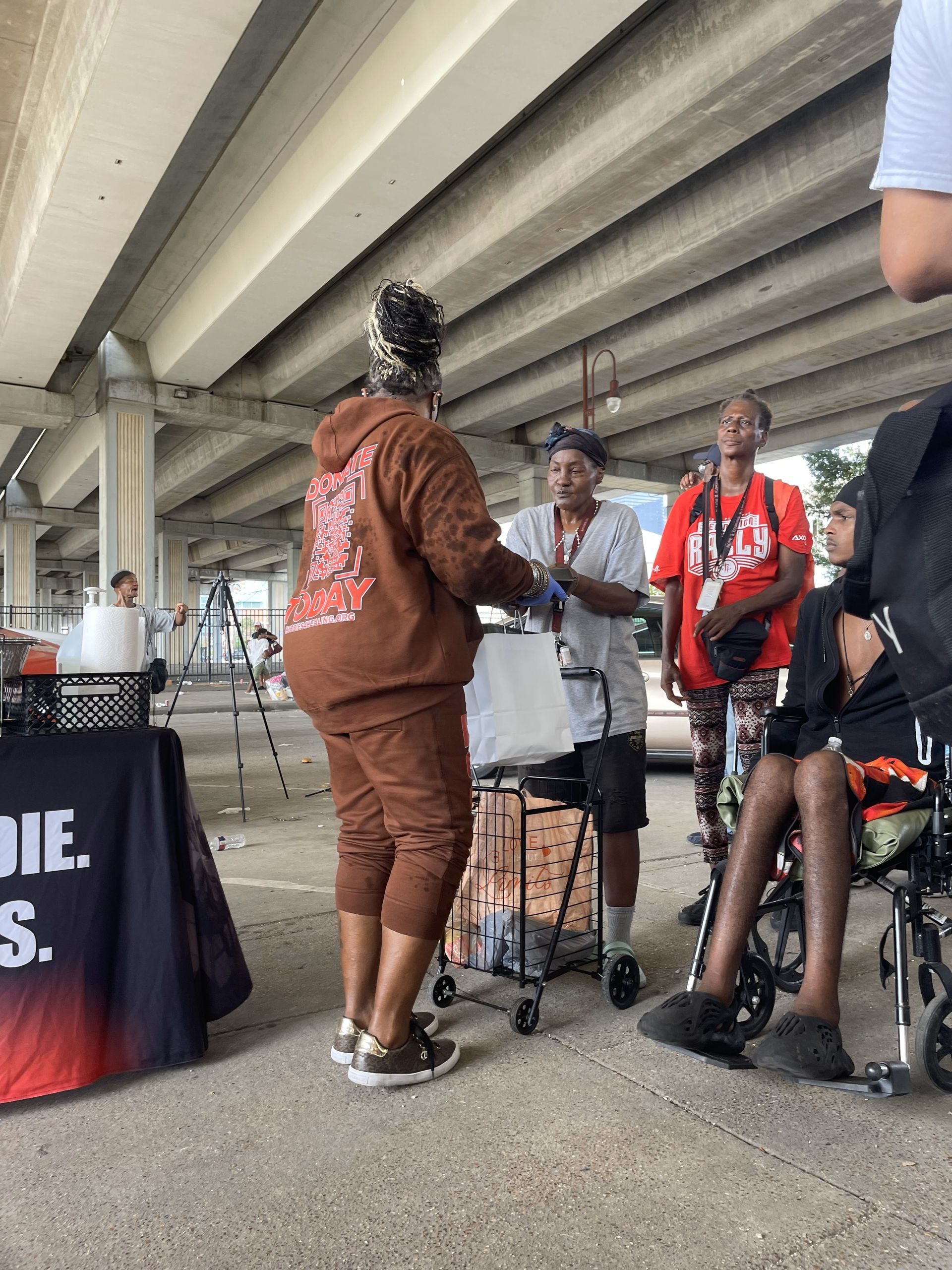 A group of people are standing around a table under a bridge.