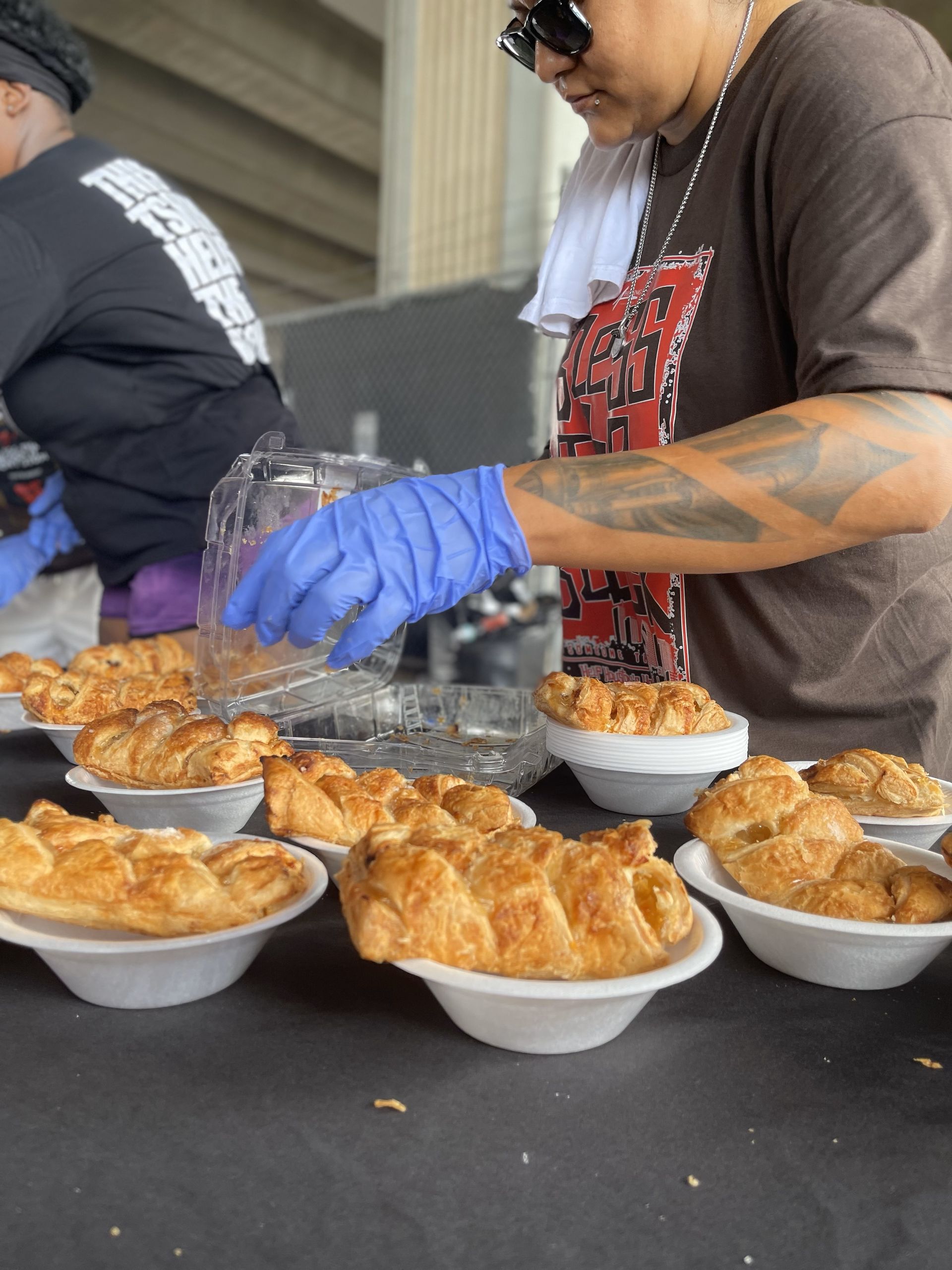 A woman in blue gloves is preparing food in bowls on a table.
