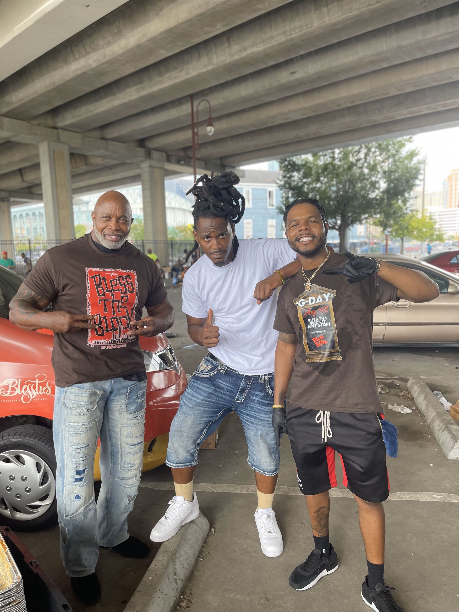 Three men are posing for a picture in a parking lot.