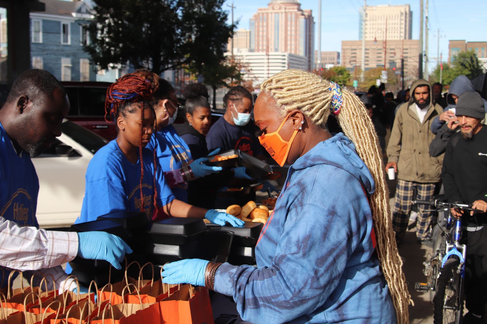 A group of people are standing around a table with bags of food.