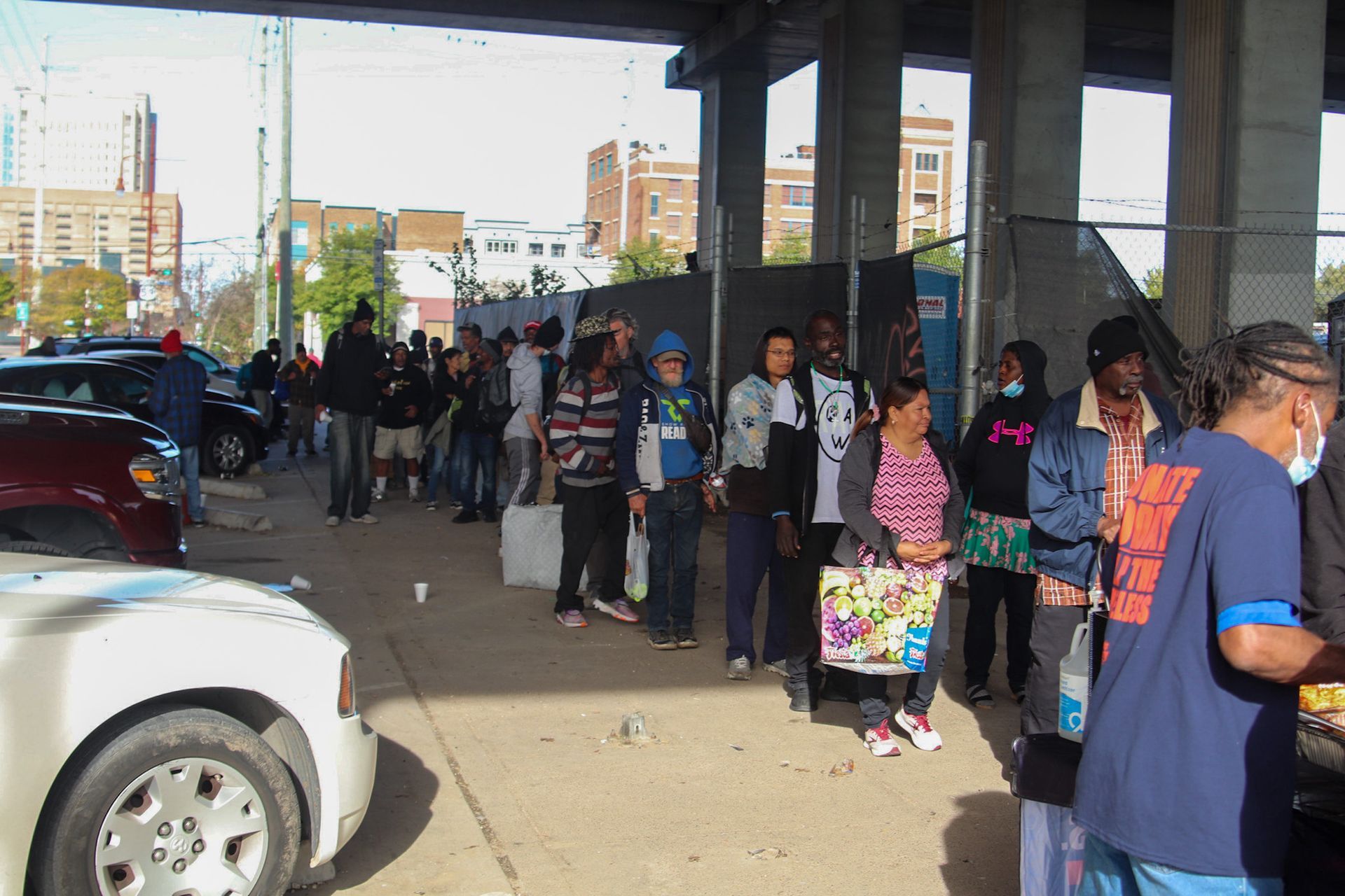 A group of people are standing in a parking lot under a bridge.