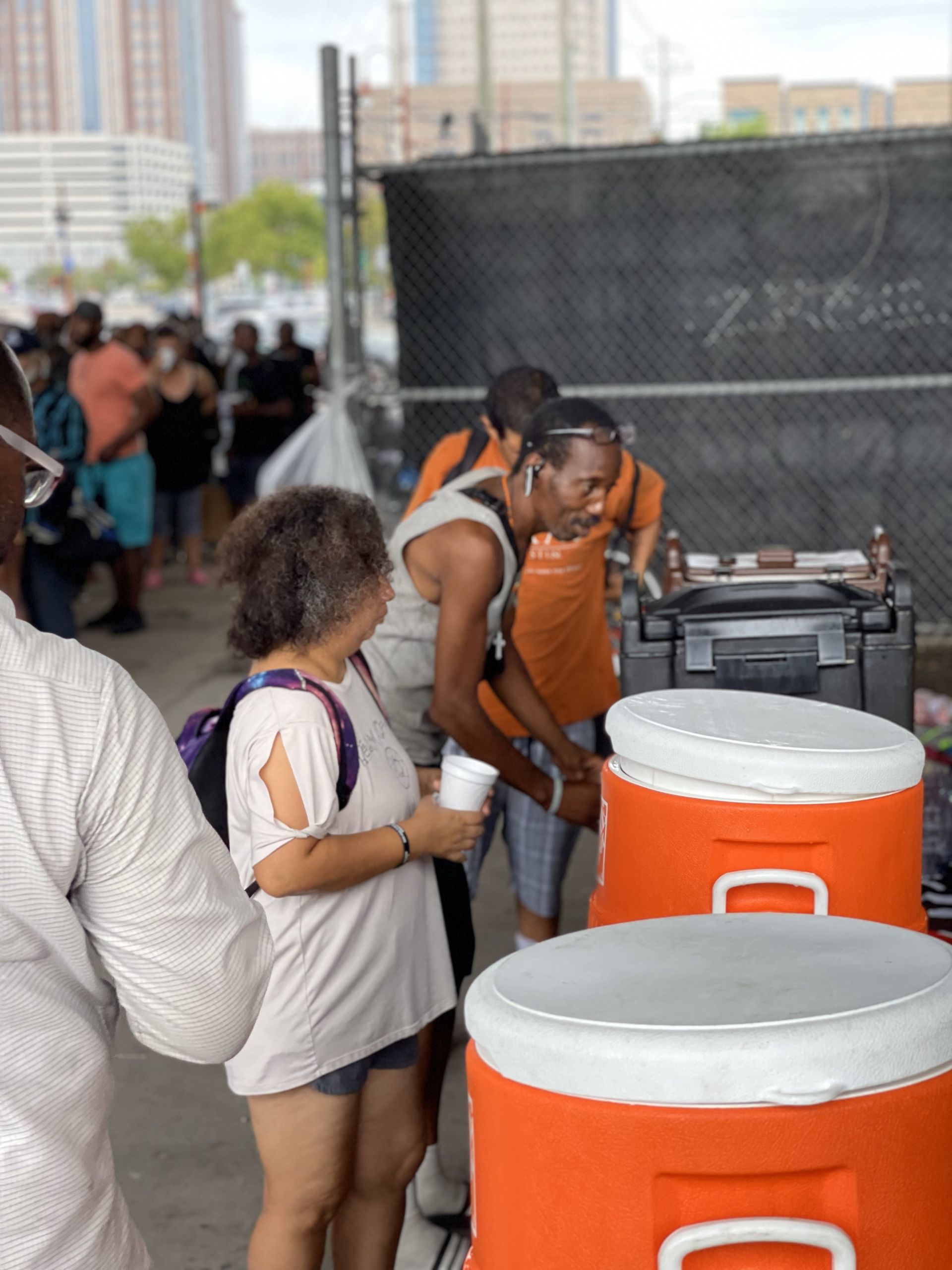 A group of people standing around orange coolers with the letter c on them