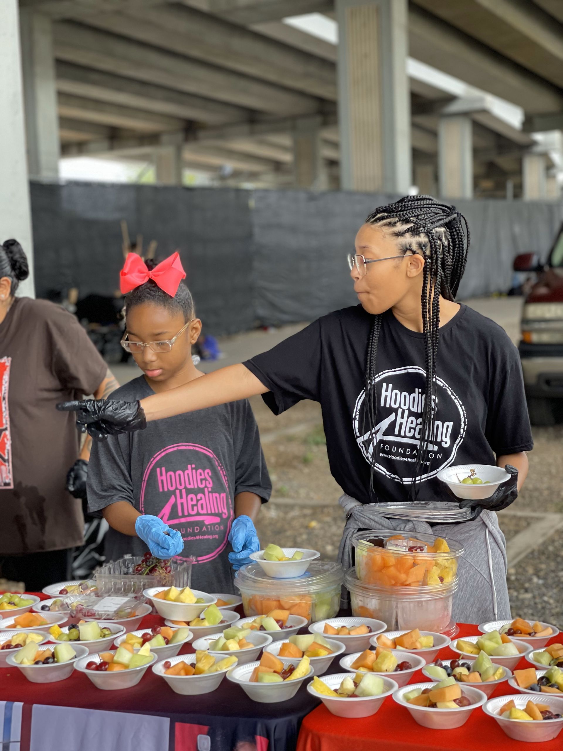 A woman and a girl are standing at a table with bowls of fruit.