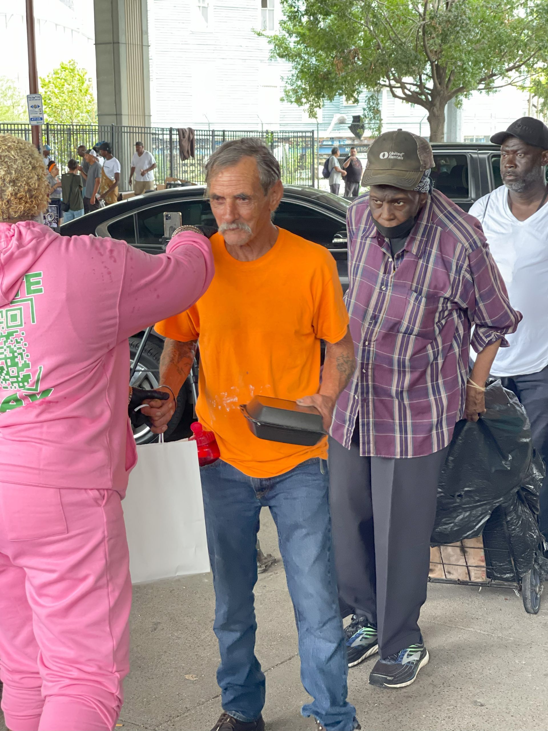 A man in an orange shirt is being helped by a woman in a pink hoodie