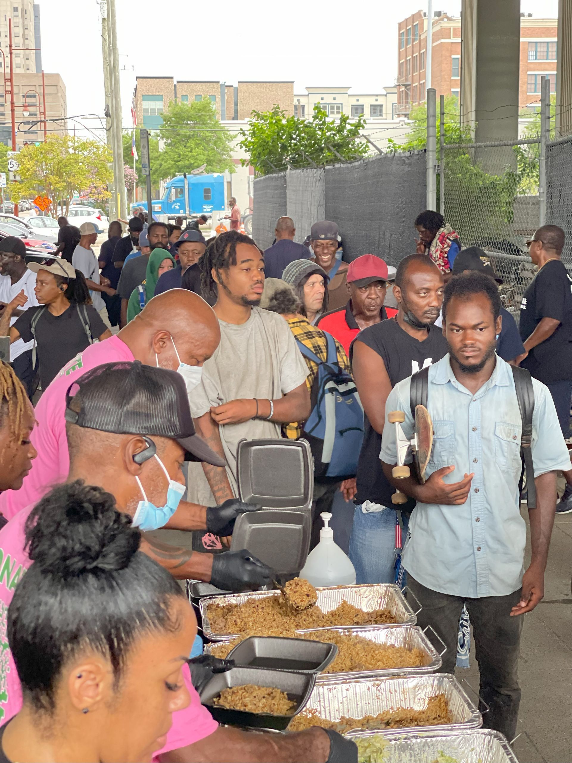 A large group of people are standing around a table filled with food.