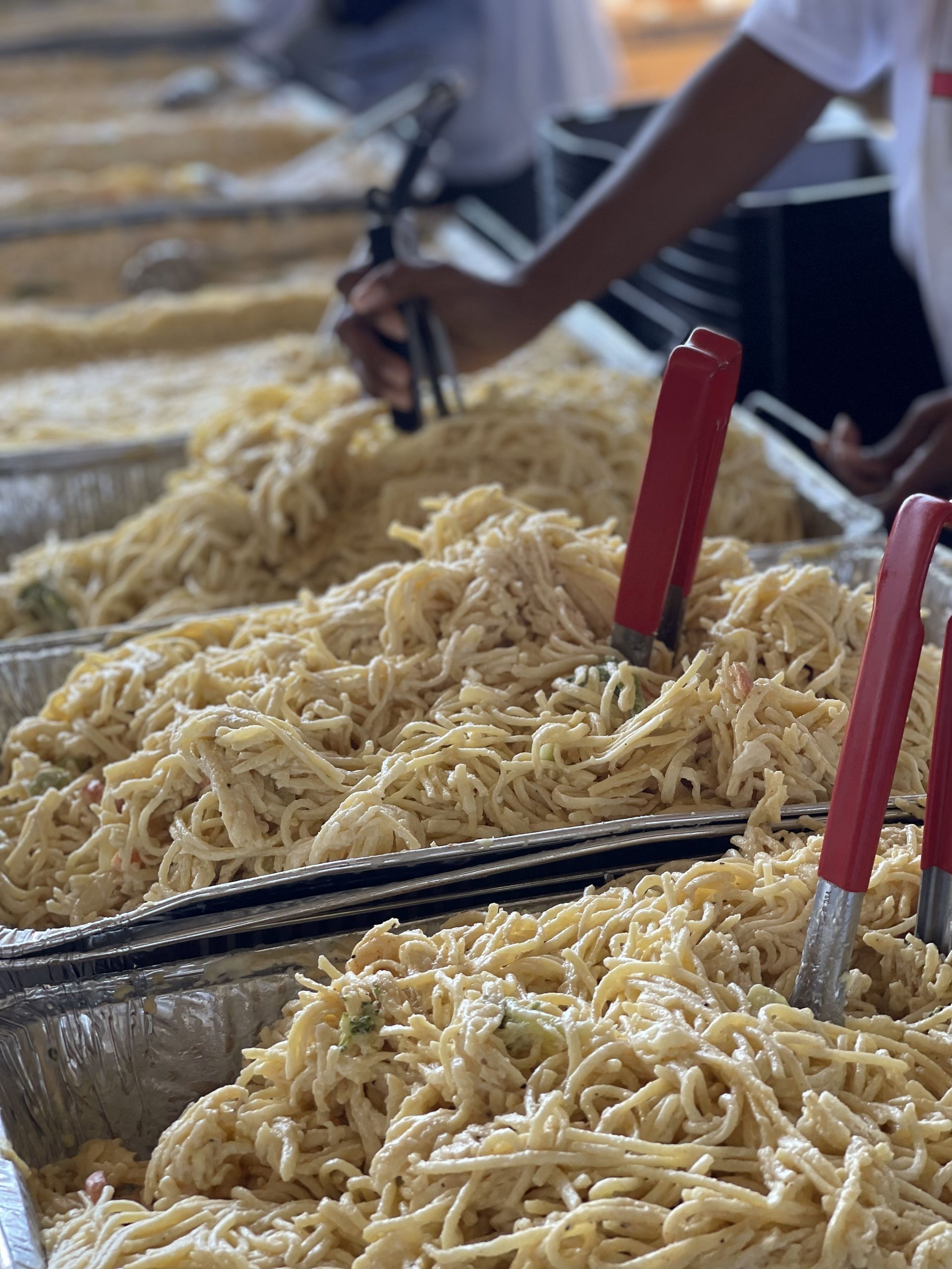 A person is holding tongs over a tray of noodles.