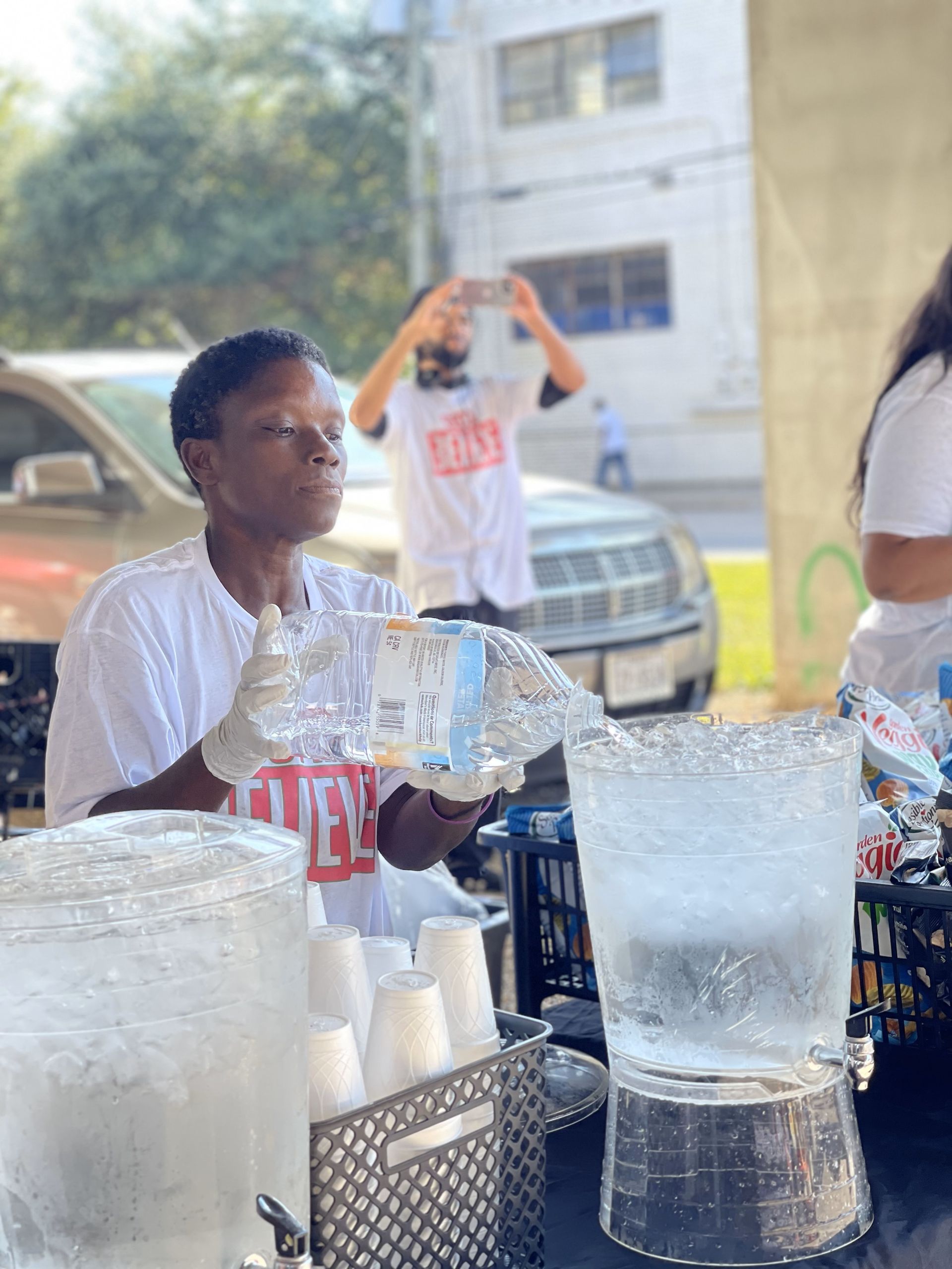 A woman is pouring water into a pitcher at a table.
