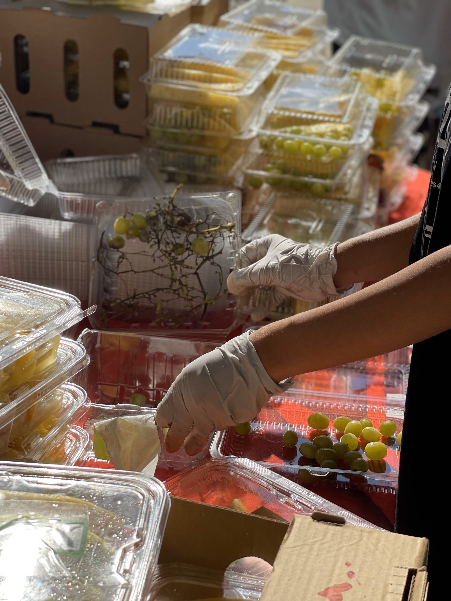 A person wearing gloves is reaching into a box of grapes.