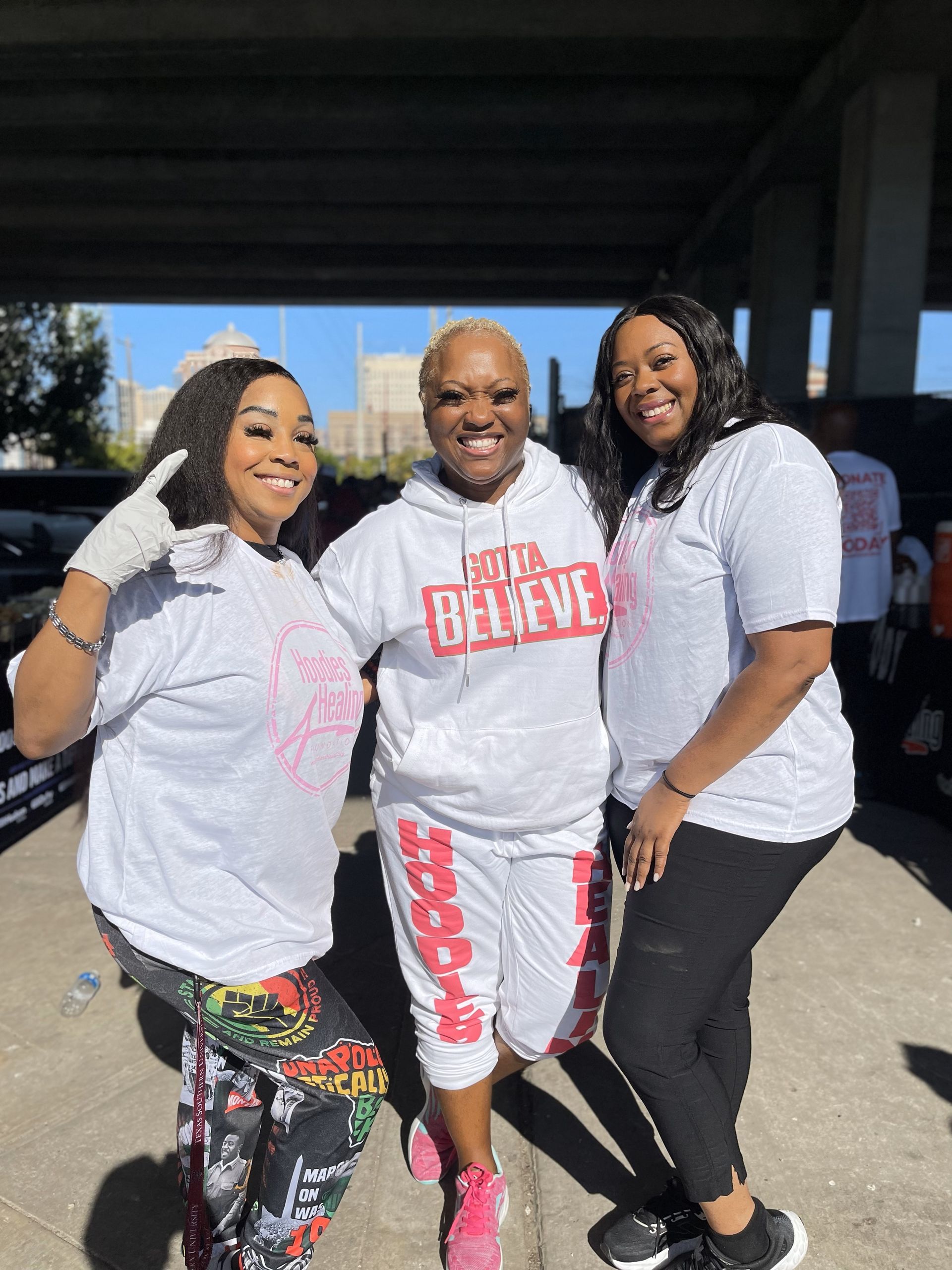 Three women are posing for a picture together in a parking lot.