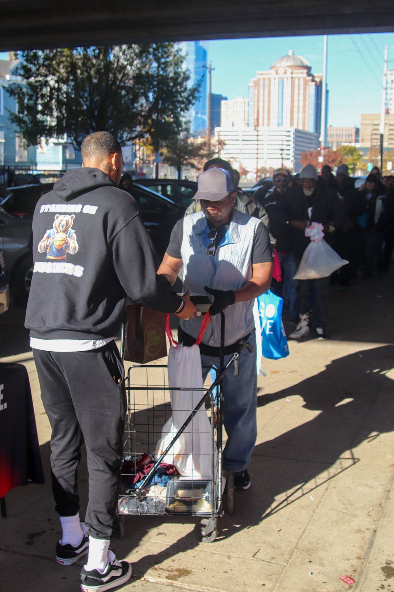 A man in a black sweatshirt with a dog on the back is shaking hands with a man in a wheelchair.