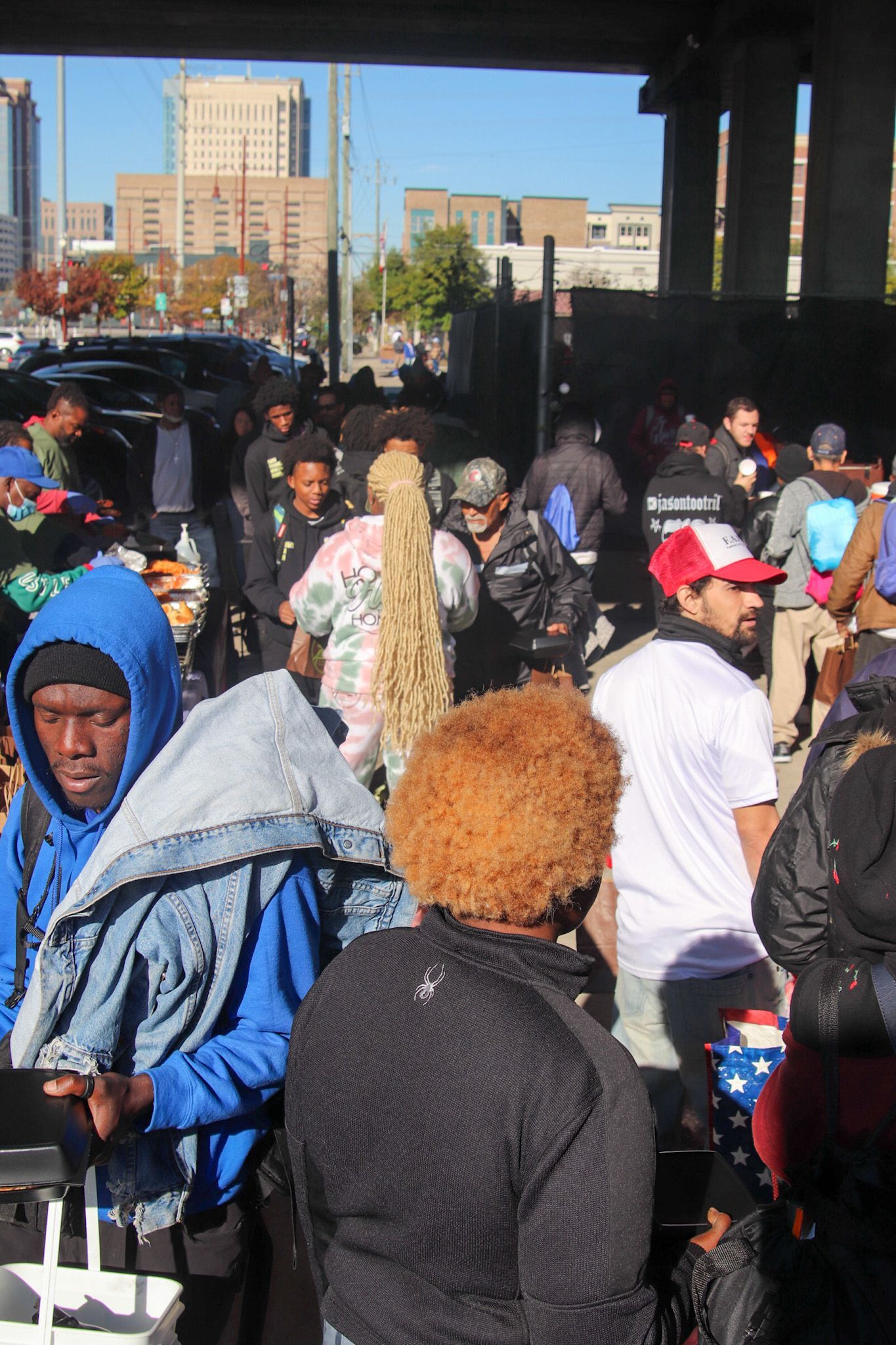 A crowd of people are gathered under a bridge in a city