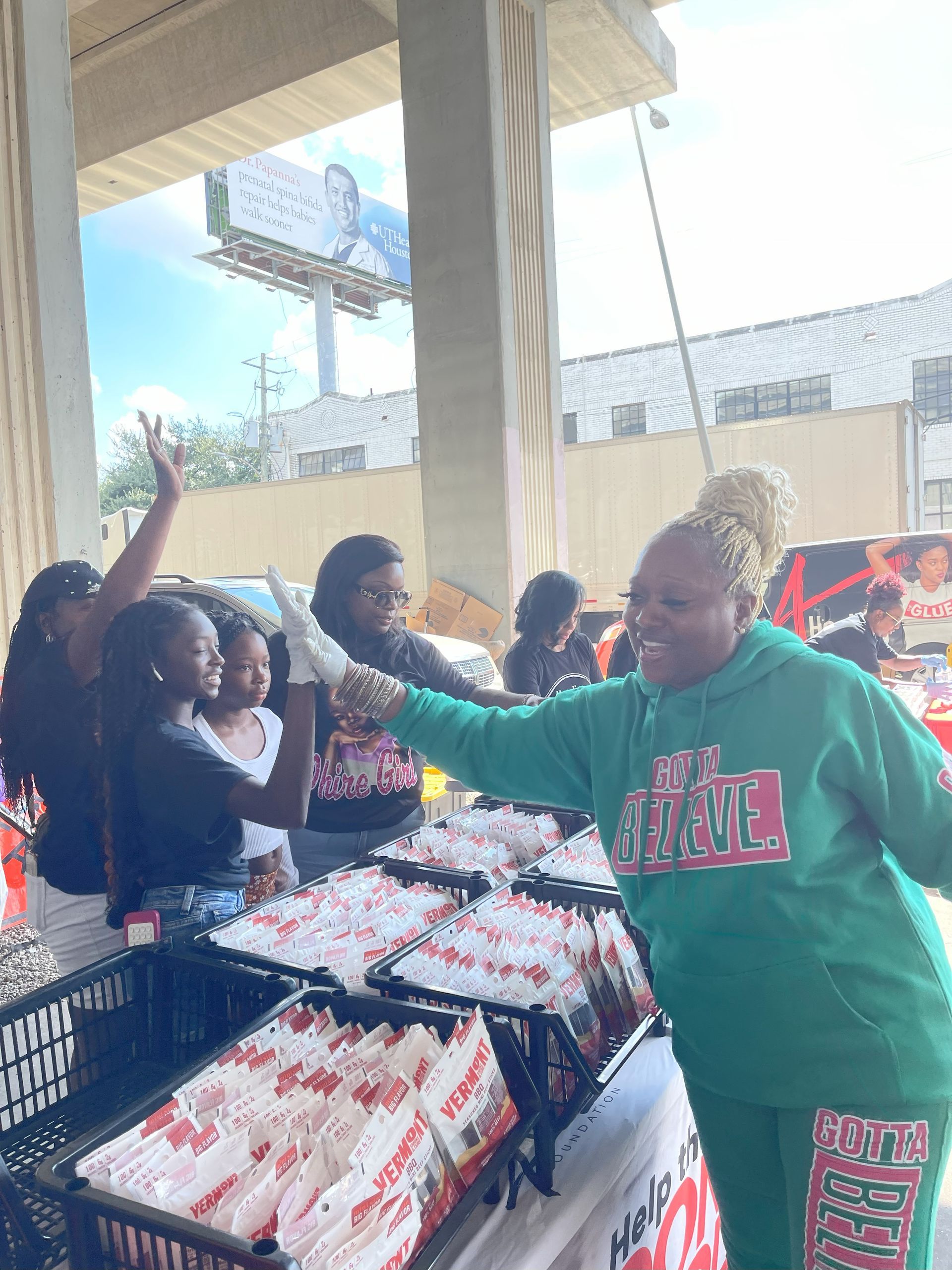 A woman in a green hoodie is standing in front of a table full of food.