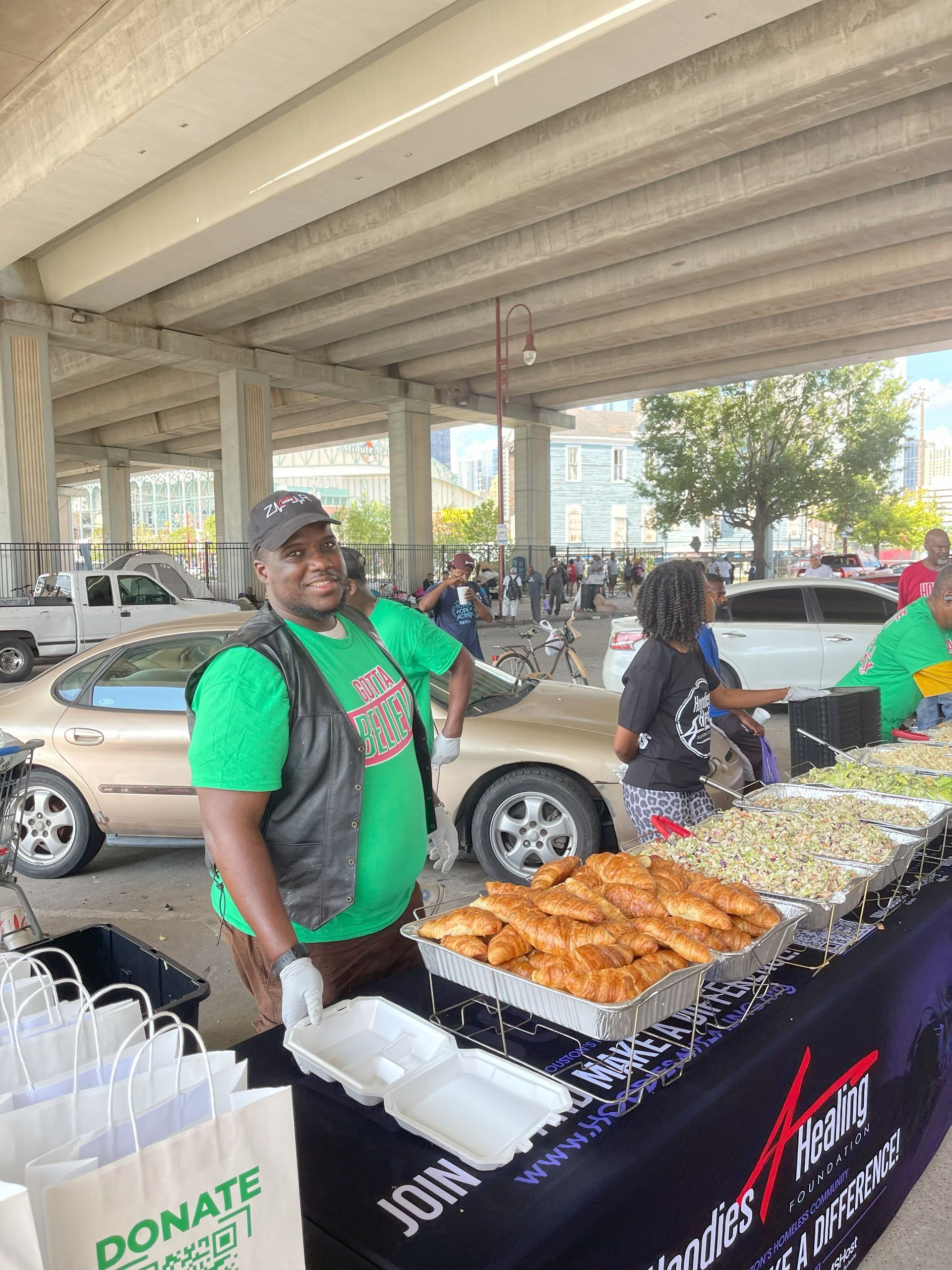 A man in a green shirt is standing in front of a table filled with food.