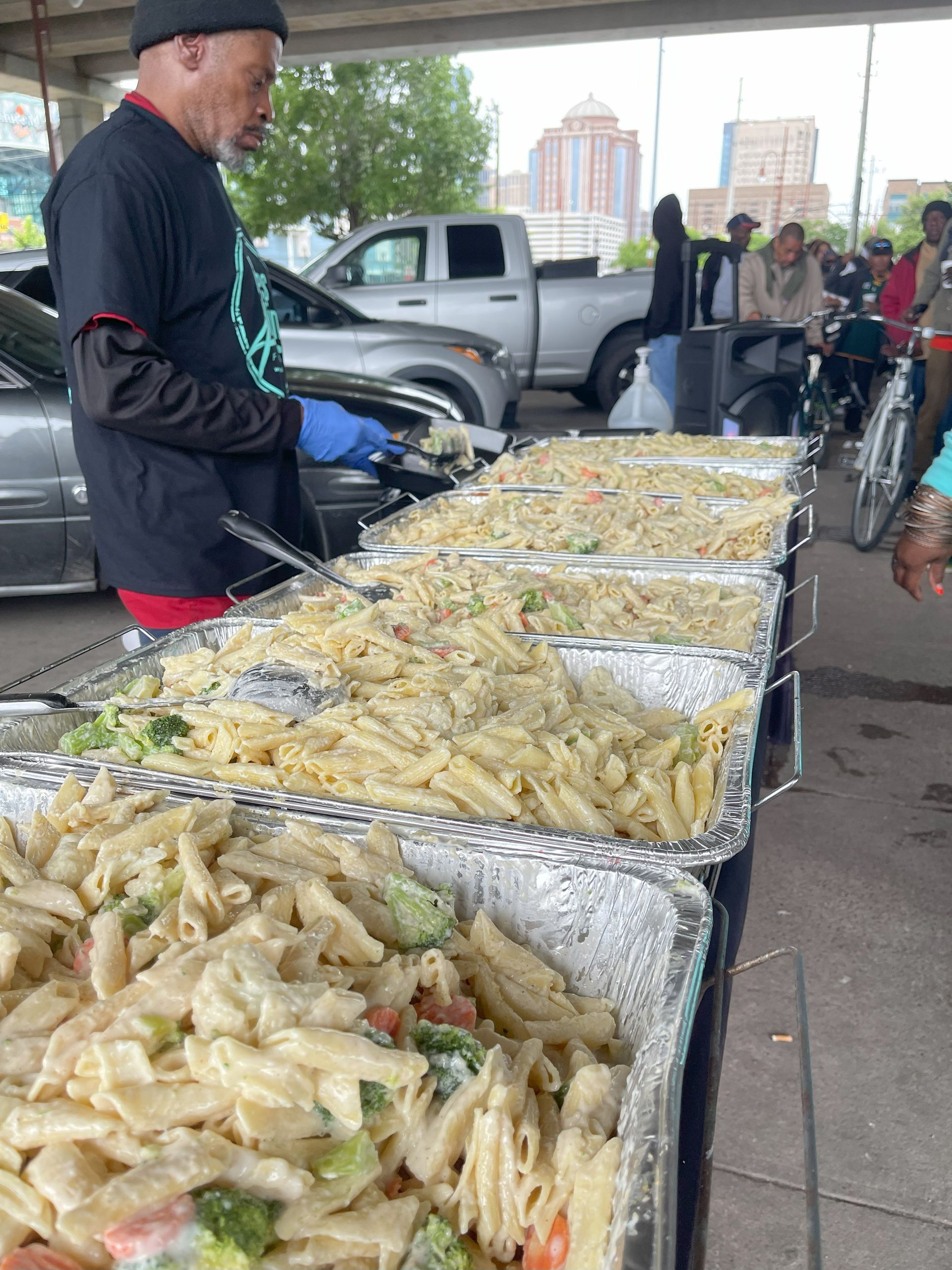 A man is standing behind a buffet line filled with pasta and vegetables.