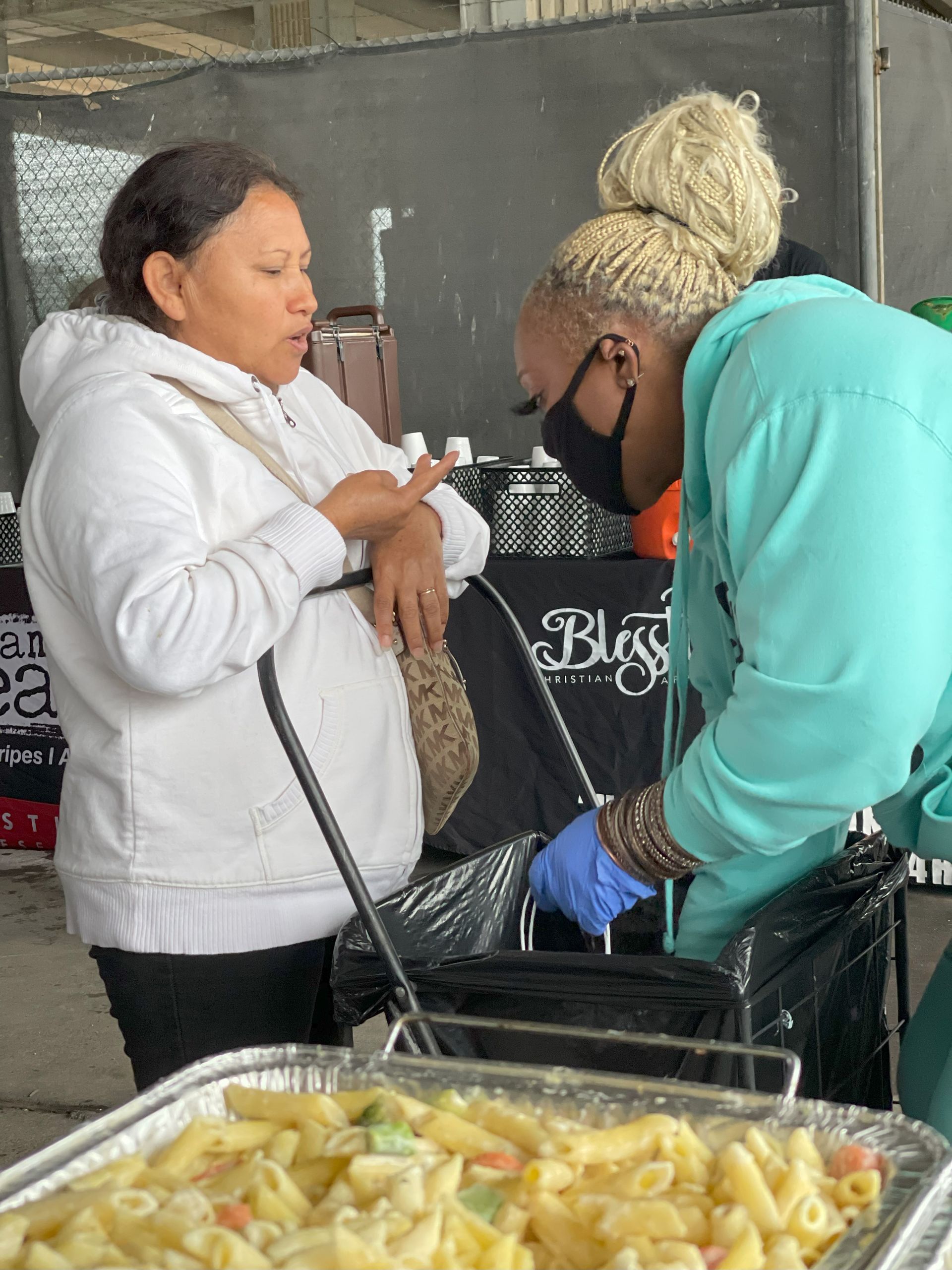 Two women are standing next to a tray of macaroni and cheese.