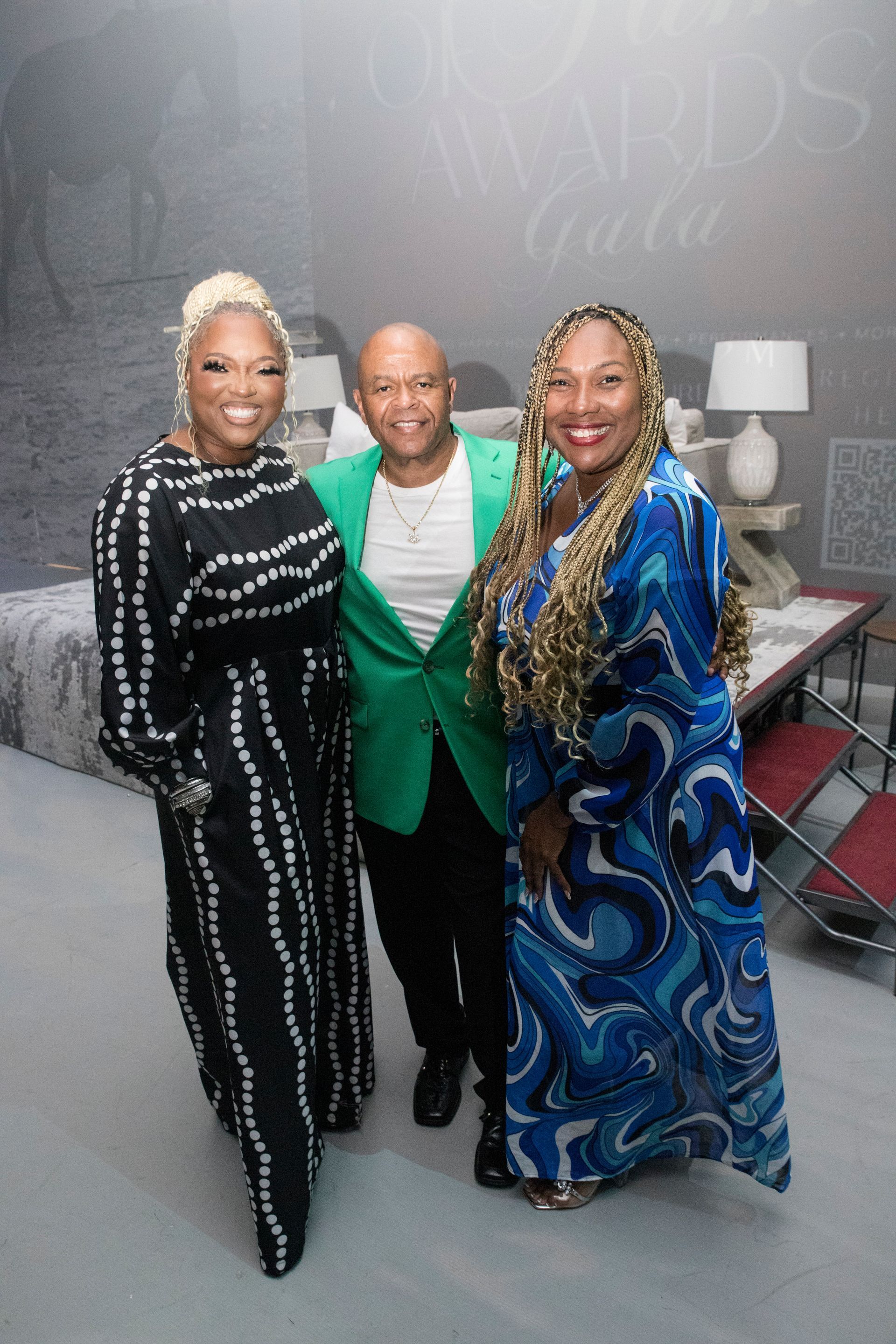 A man in a green jacket is standing next to two women in blue dresses.