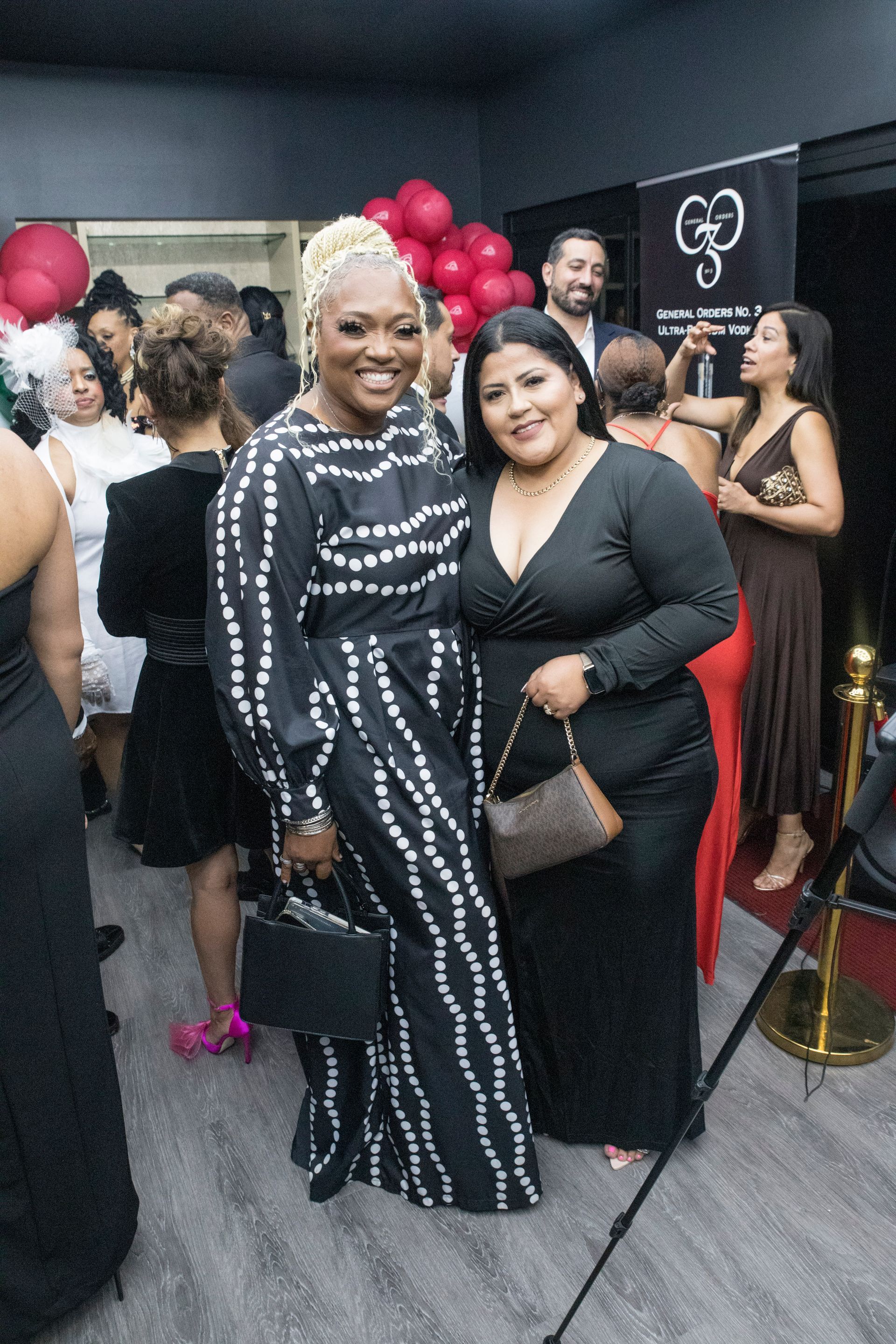 Two women in black dresses are posing for a picture at a party.