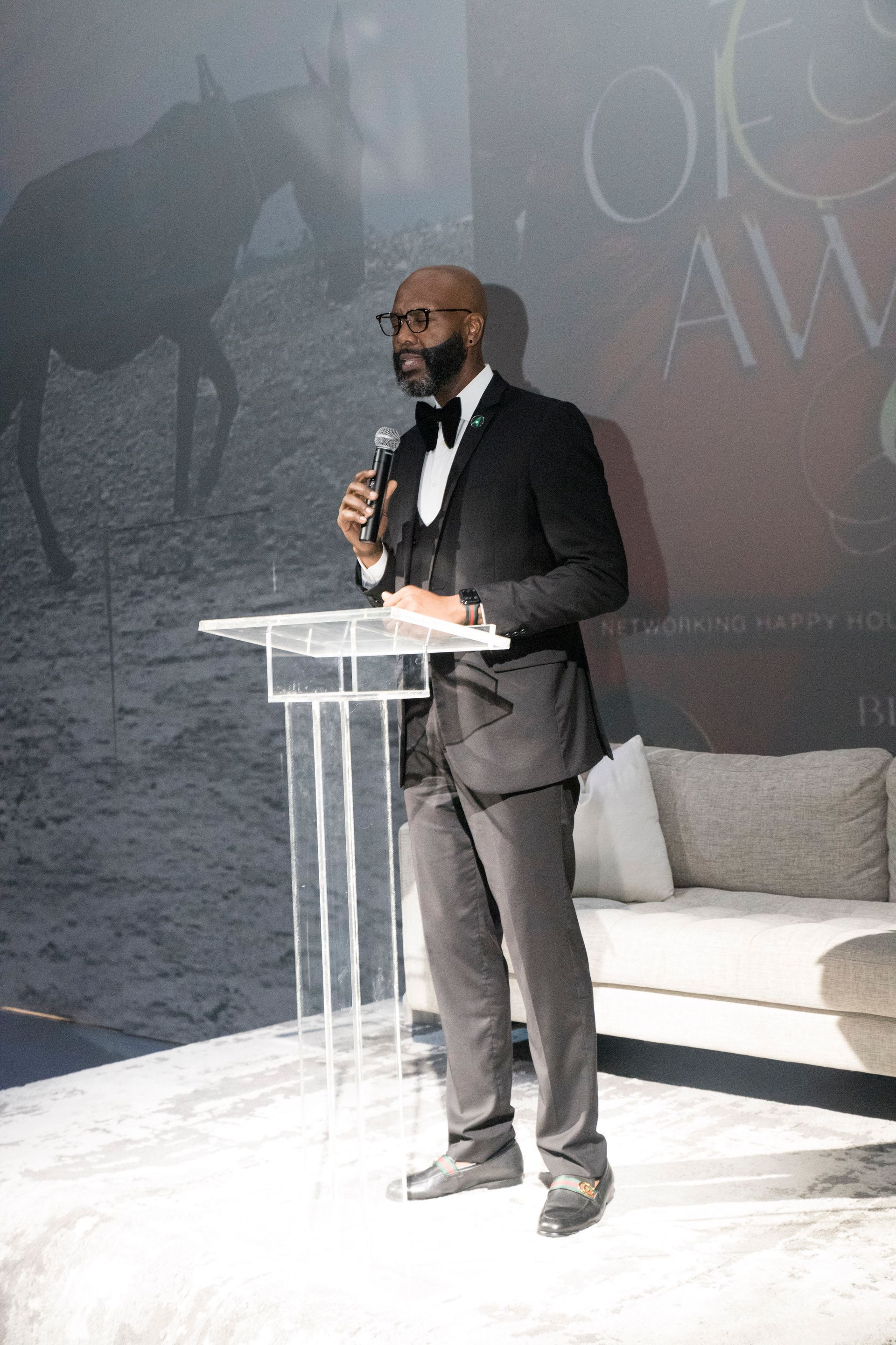 A man in a tuxedo is standing at a podium holding a microphone.