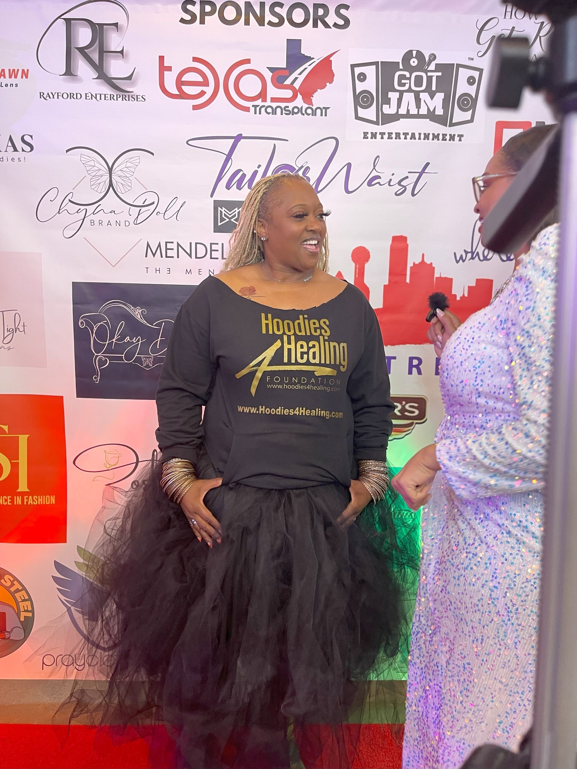 A woman is standing on a red carpet talking to another woman.