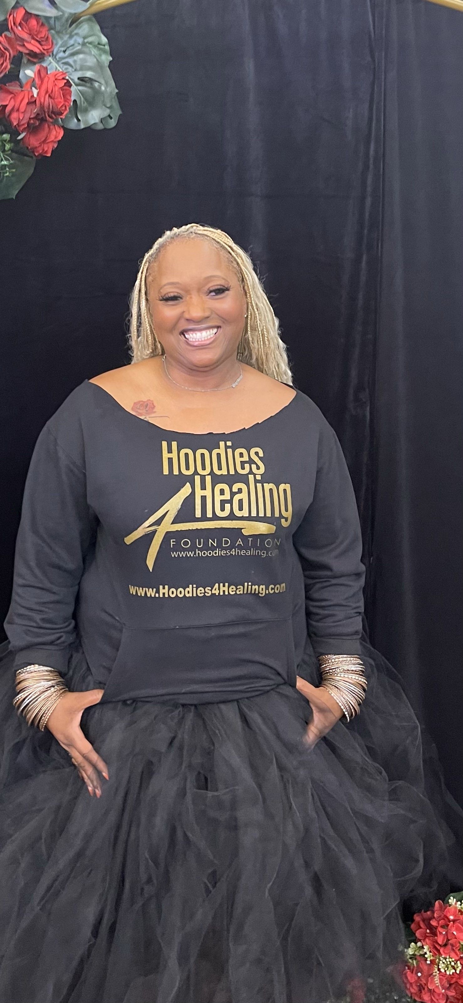 A woman wearing a black shirt and a black skirt is standing in front of a black curtain.