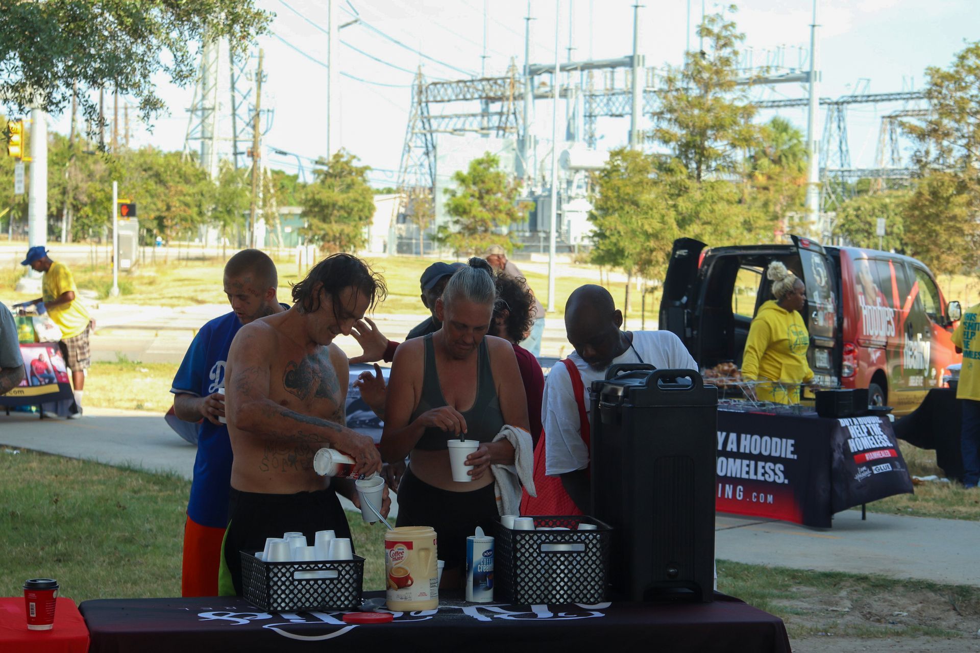 A group of people standing around a table with a van in the background that says wireless