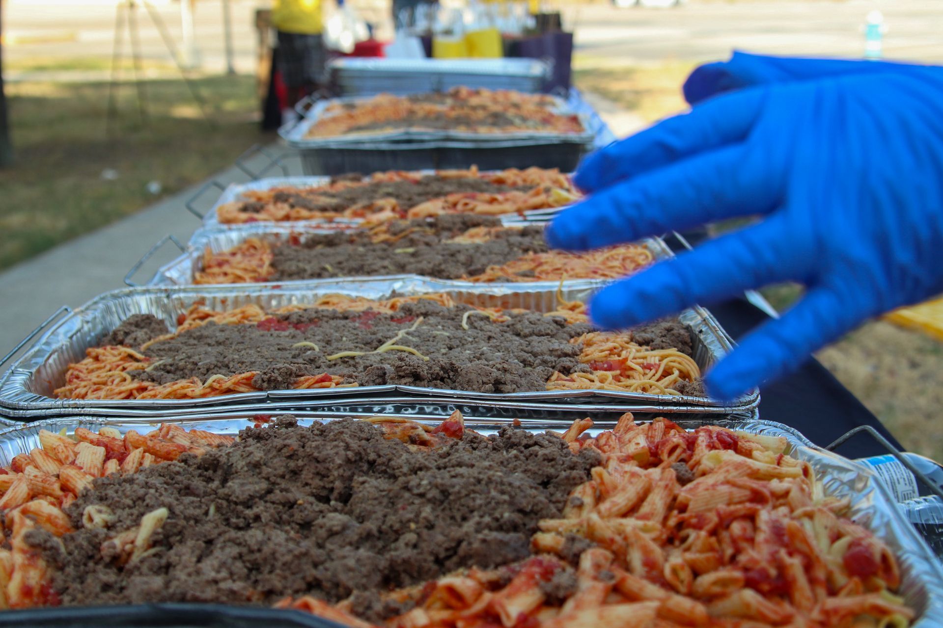 A person wearing blue gloves is reaching for a tray of food.