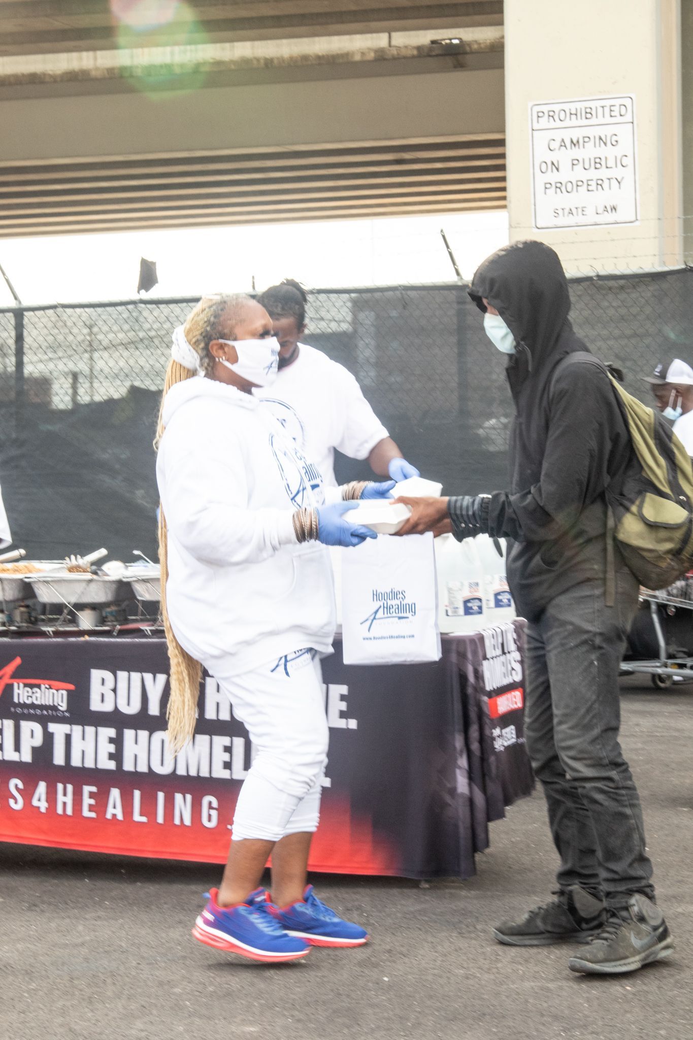 A man wearing a mask is giving a bag of food to a woman wearing a mask.