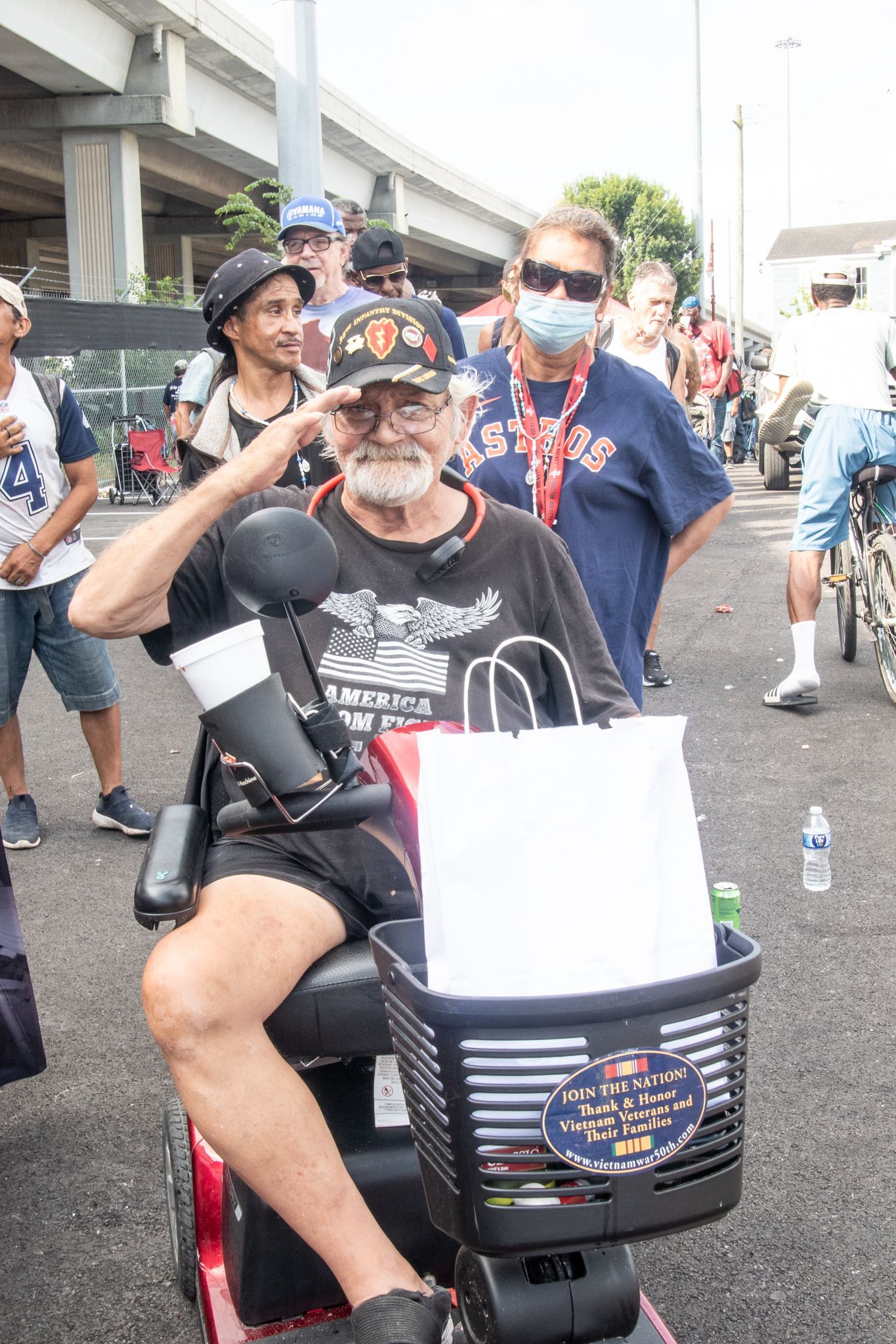 A man in a wheelchair is saluting while holding a bag.