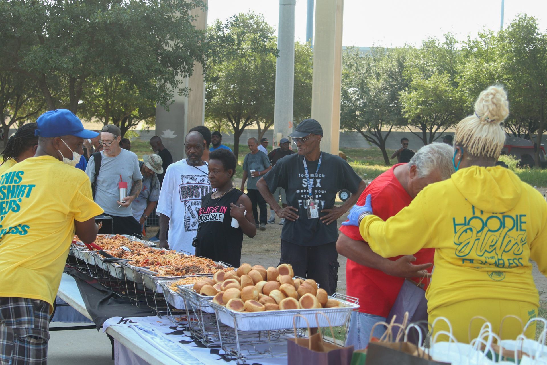 A group of people are standing around a table with food and one of them is wearing a yellow shirt that says hoodie