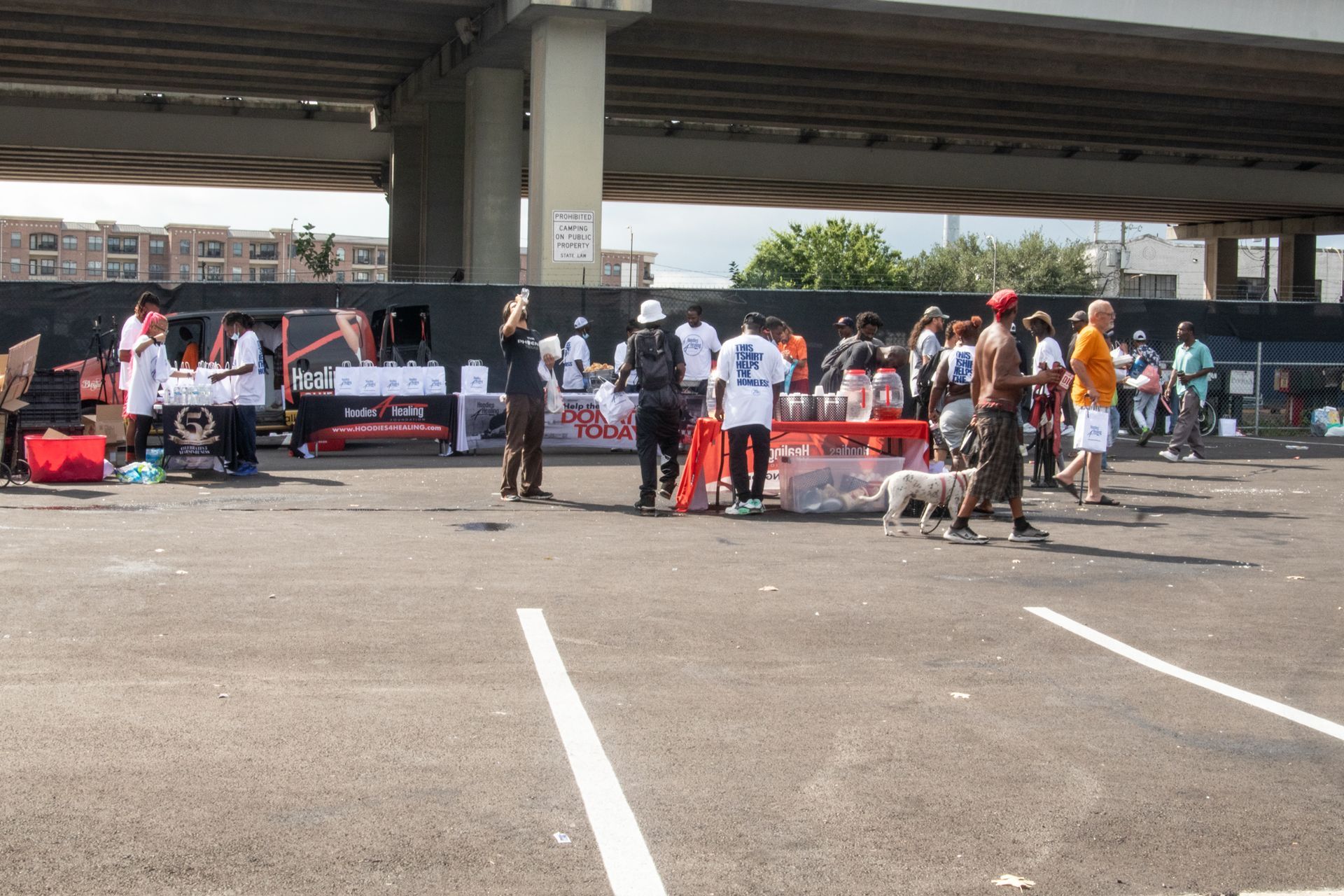 A group of people are gathered in a parking lot under a bridge
