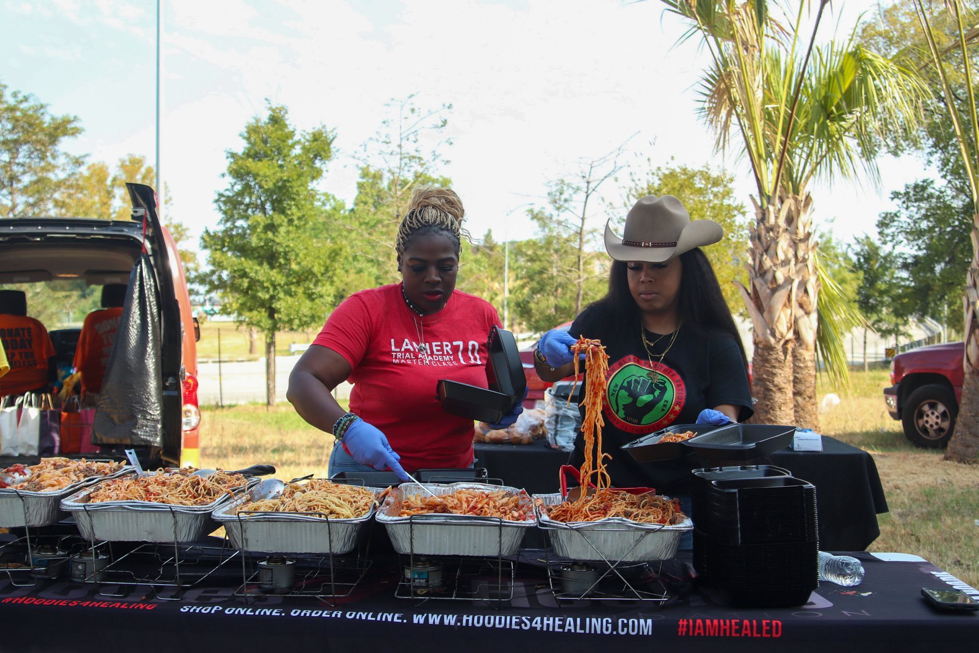 Two women are preparing food at a table in a park.