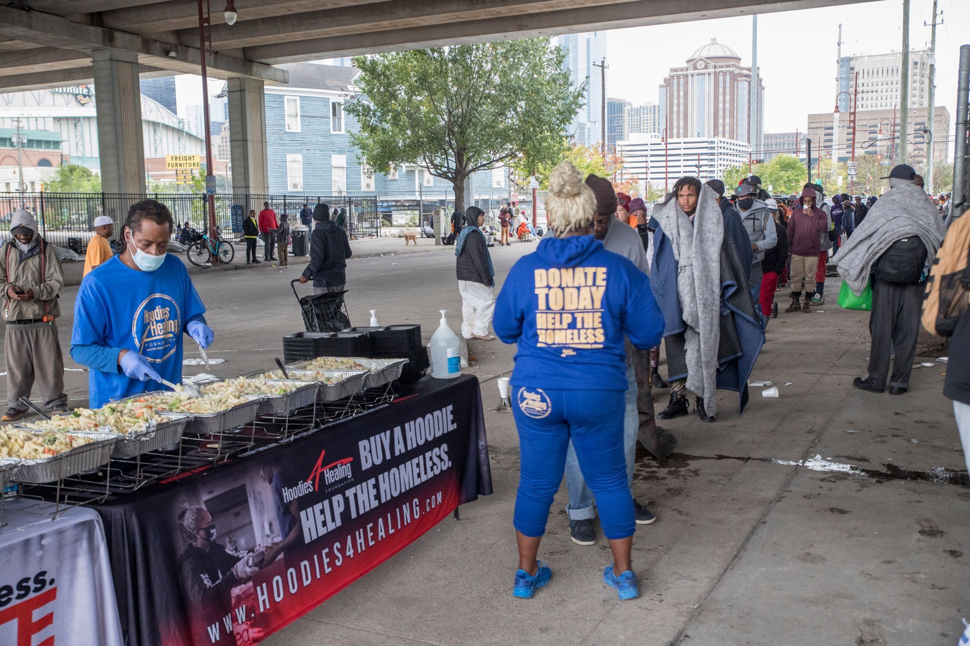 A group of people are standing around a table with food on it.