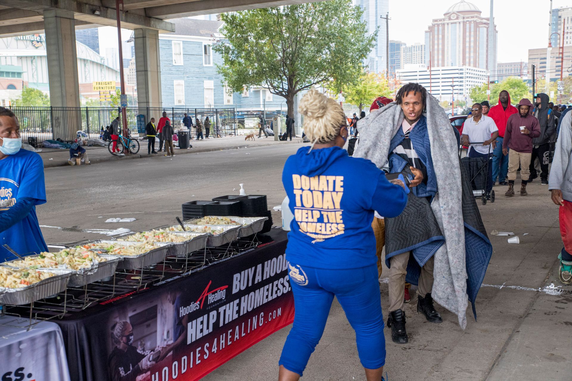 A woman in a blue hoodie is standing in front of a table with food.