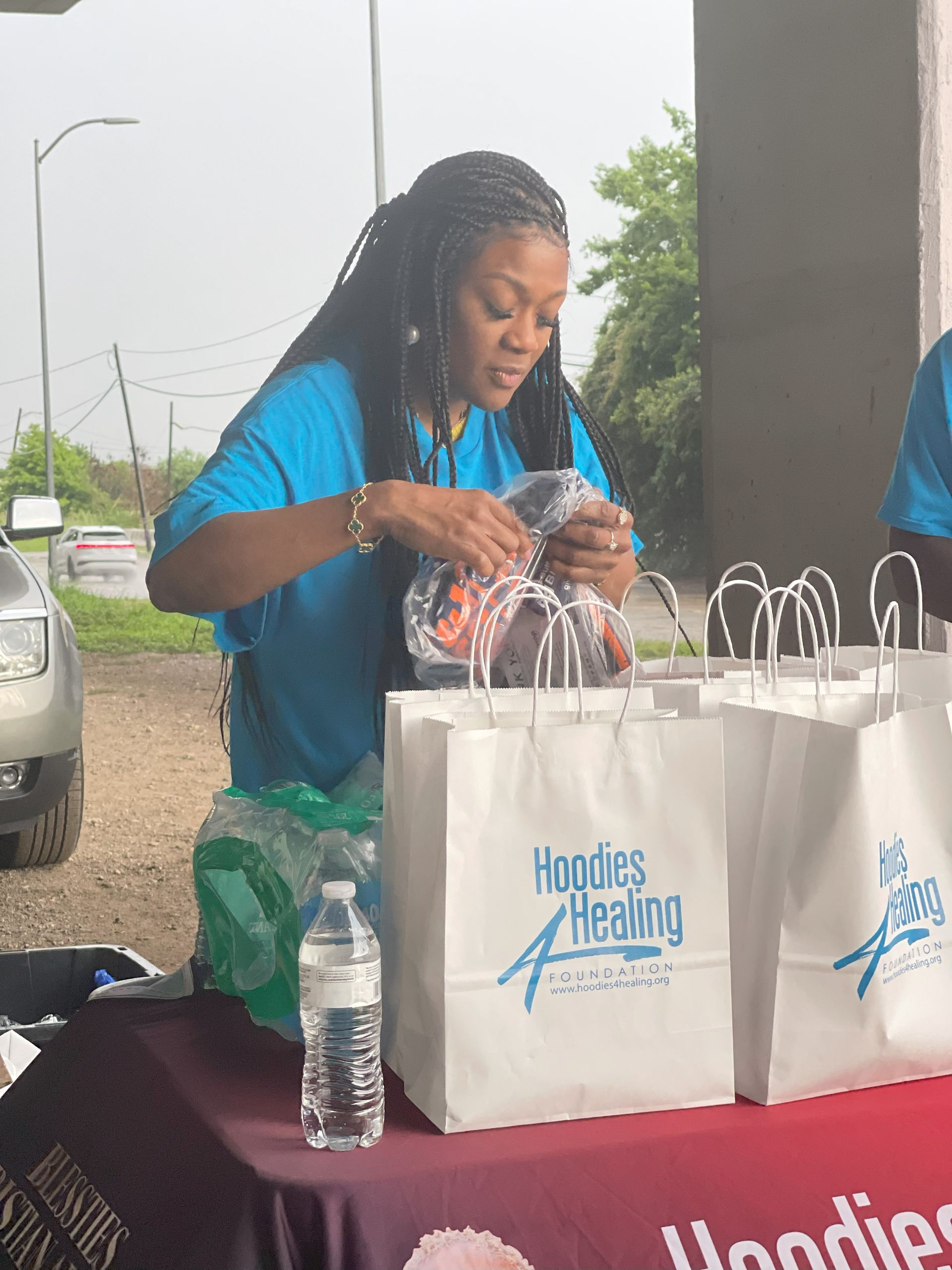 A woman in a blue shirt is standing at a table with bags on it.