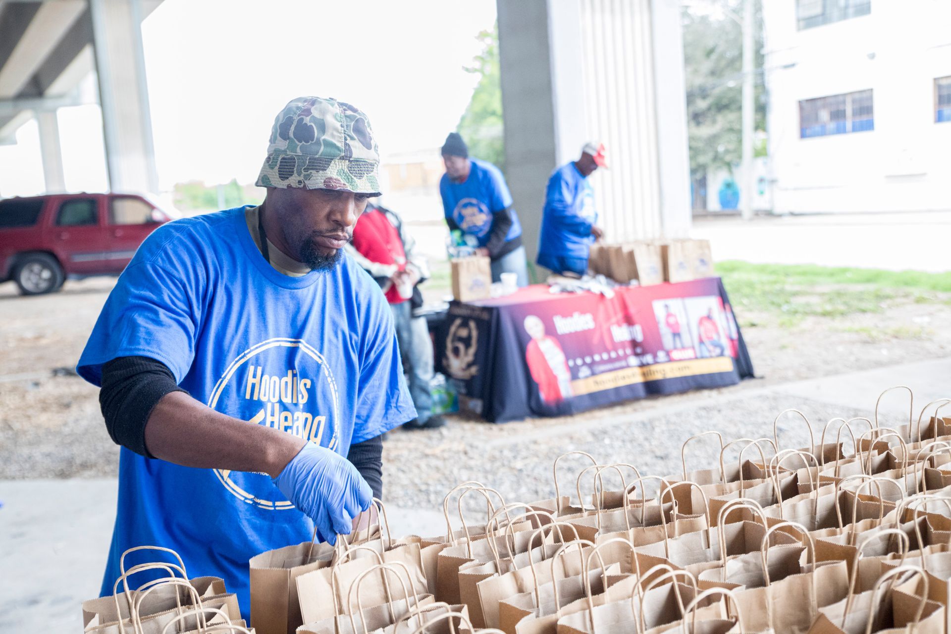 A man in a blue shirt is standing in front of a table filled with paper bags.