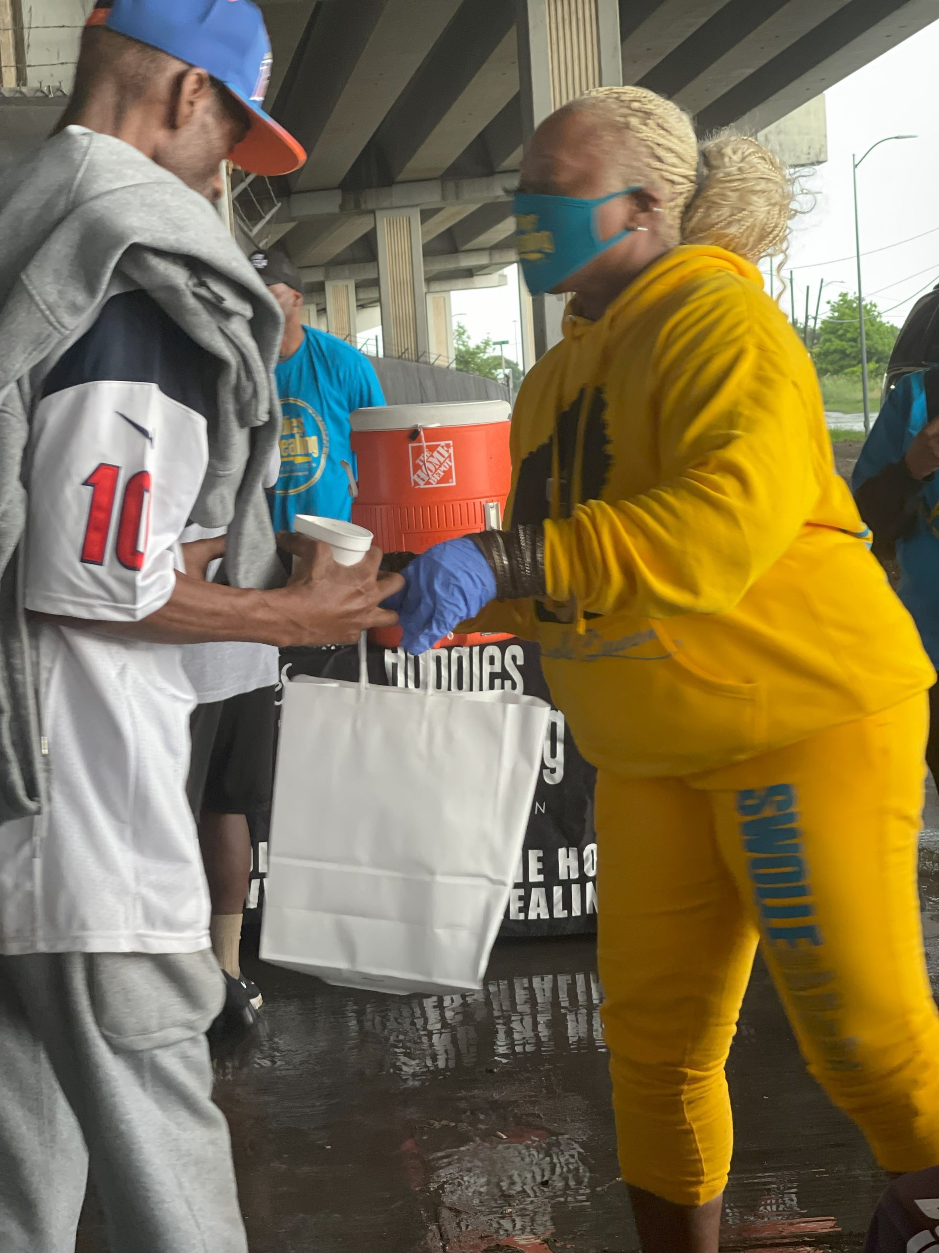 A woman wearing a mask is giving a man a cup of coffee