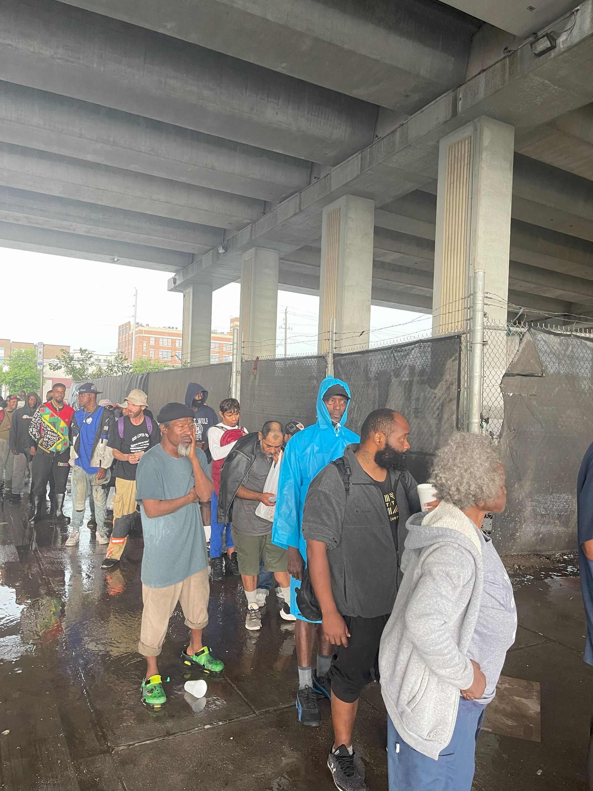 A group of people are standing under a bridge in the rain.