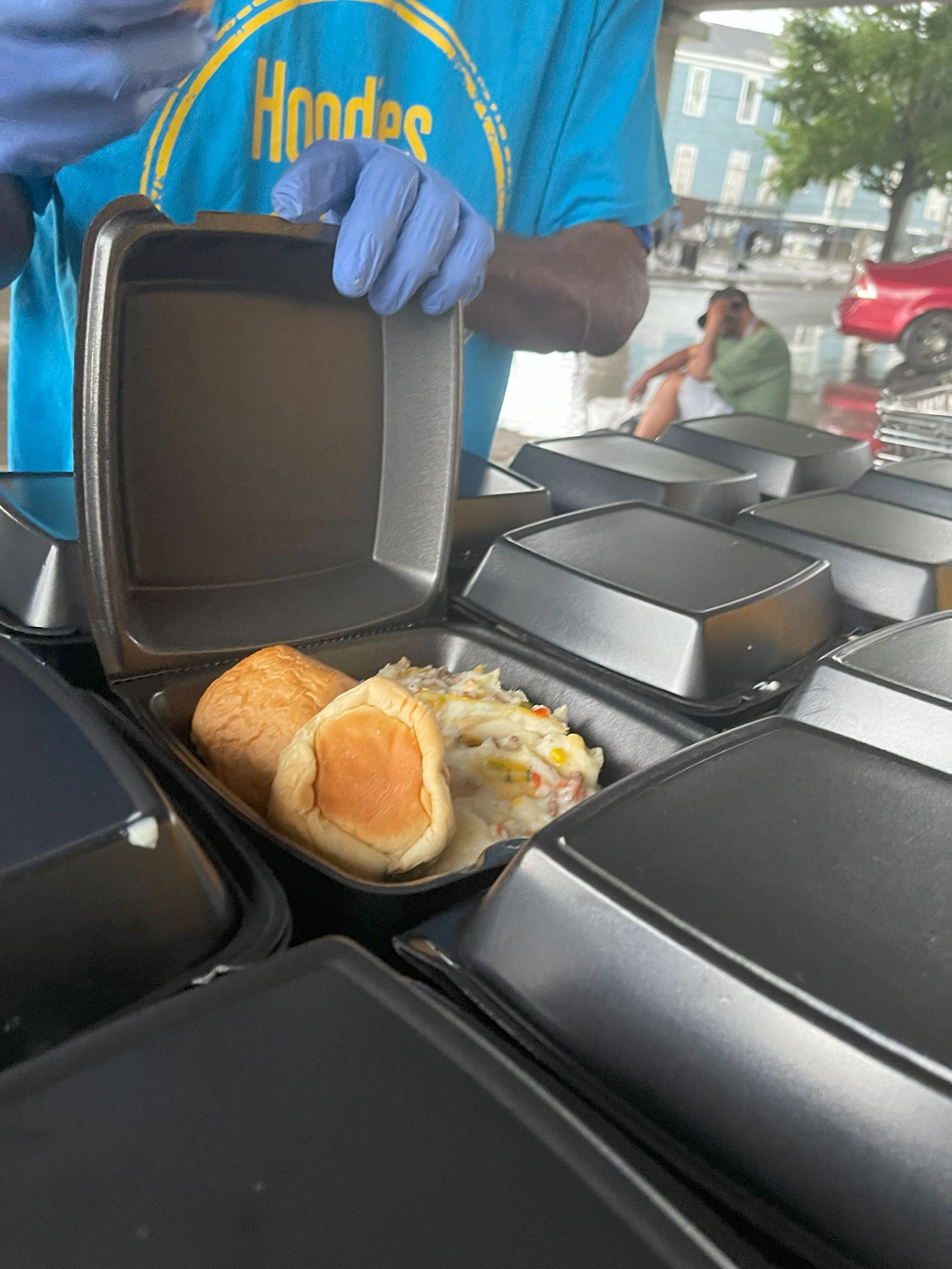 A man wearing blue gloves is opening a styrofoam container filled with food.