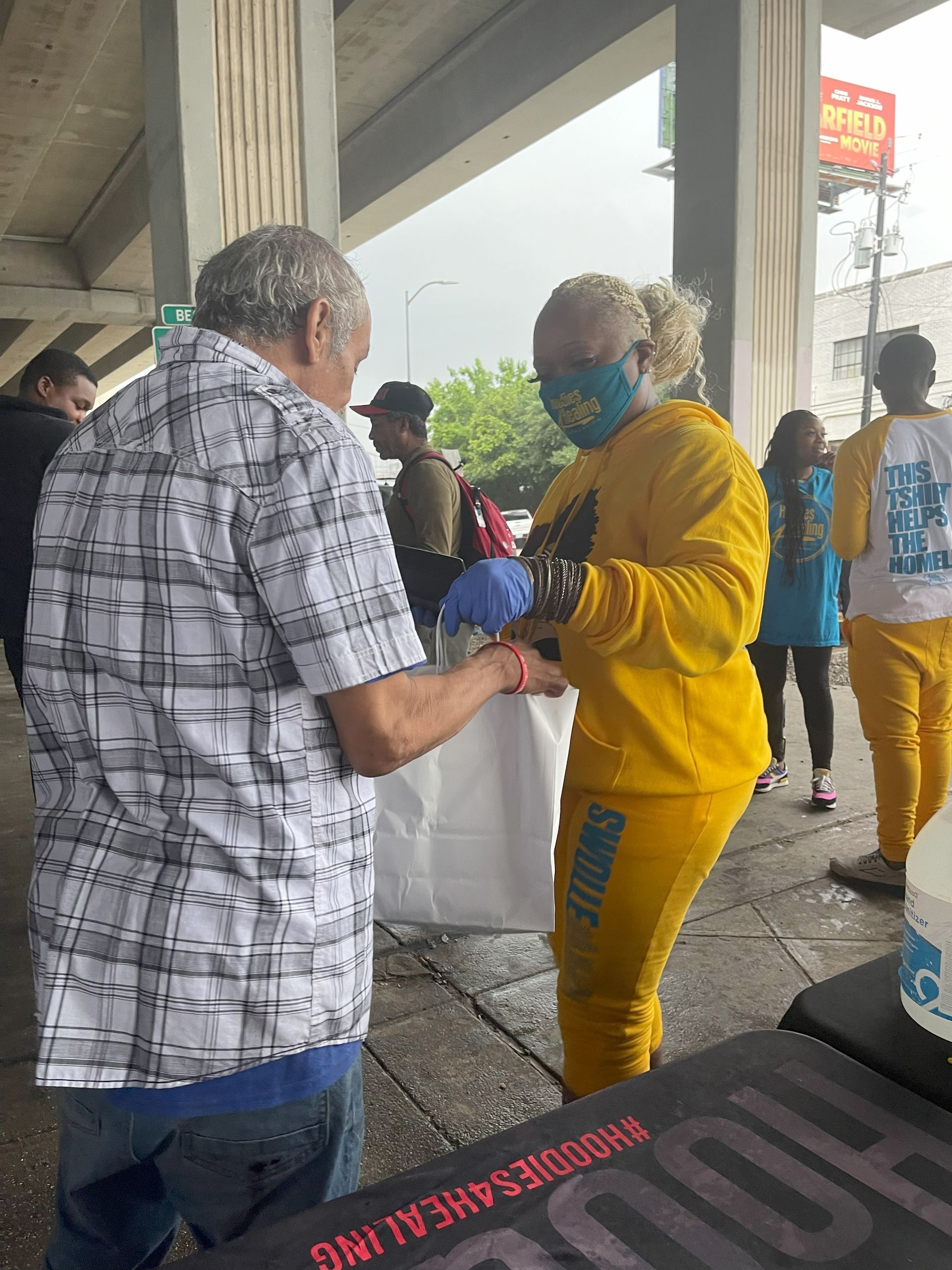 A woman wearing a mask is giving a man a bag of food.