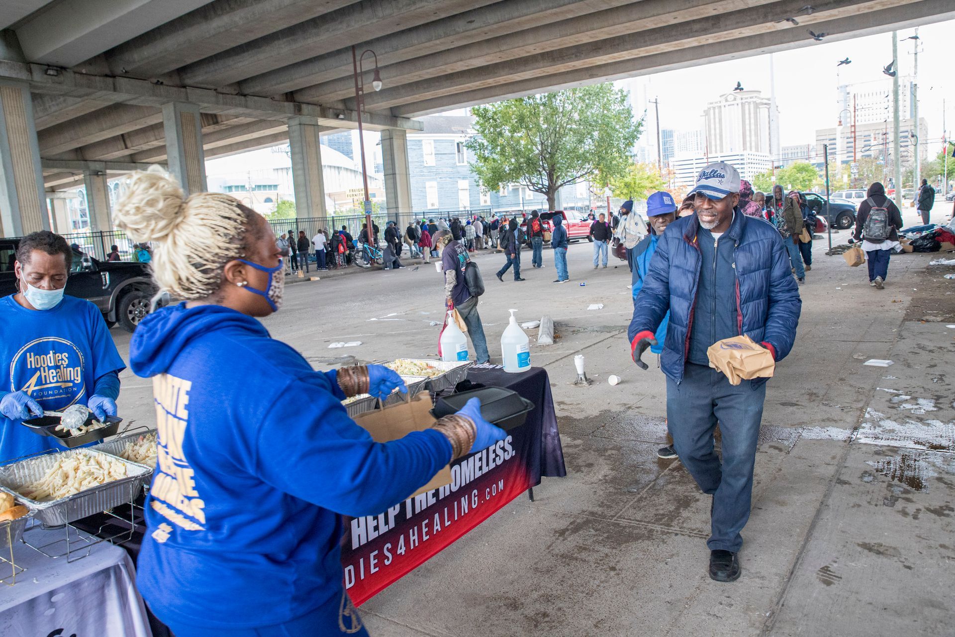 A woman is serving food to a man under a bridge.
