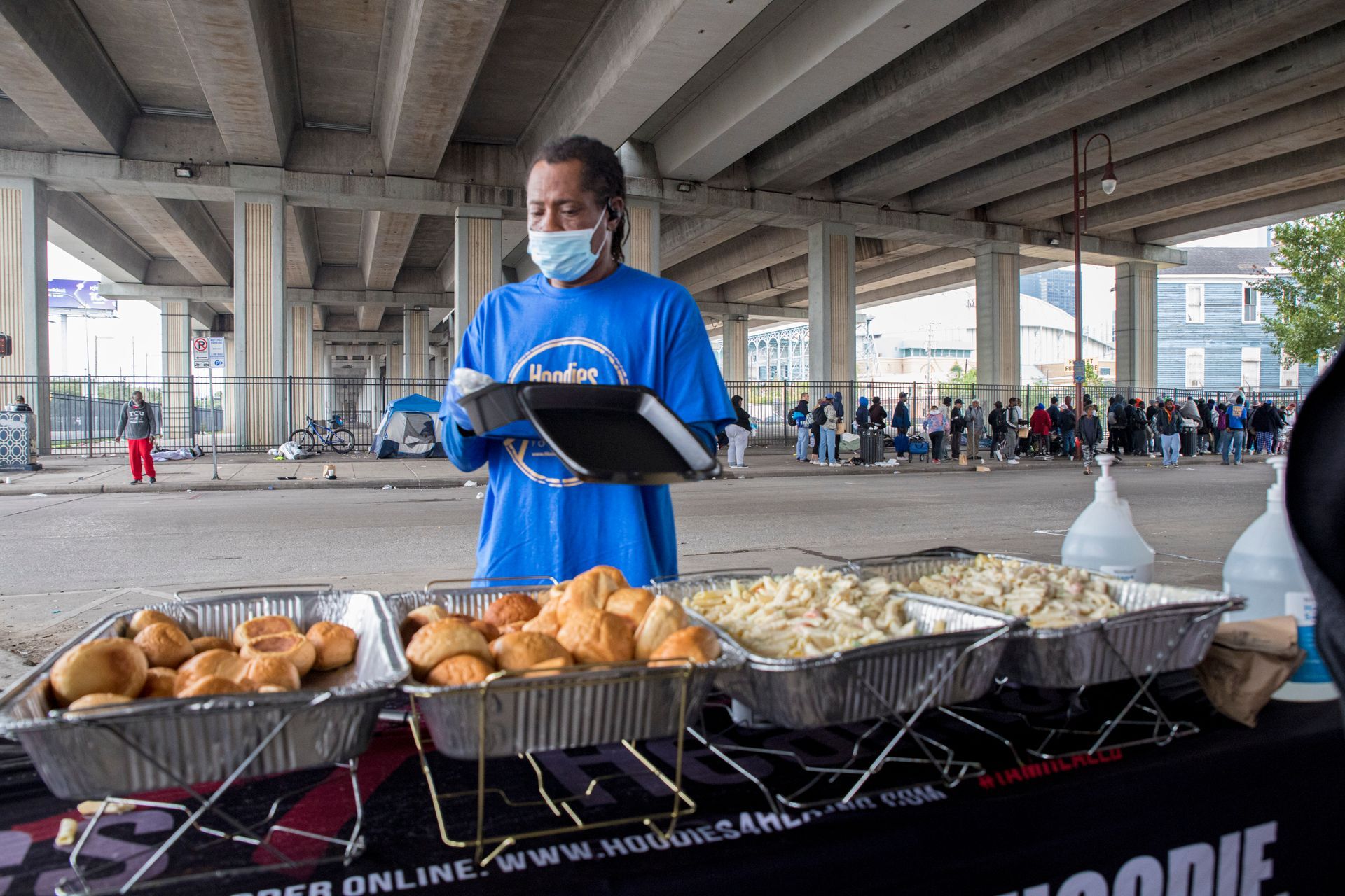 A man wearing a mask is serving food under a bridge.
