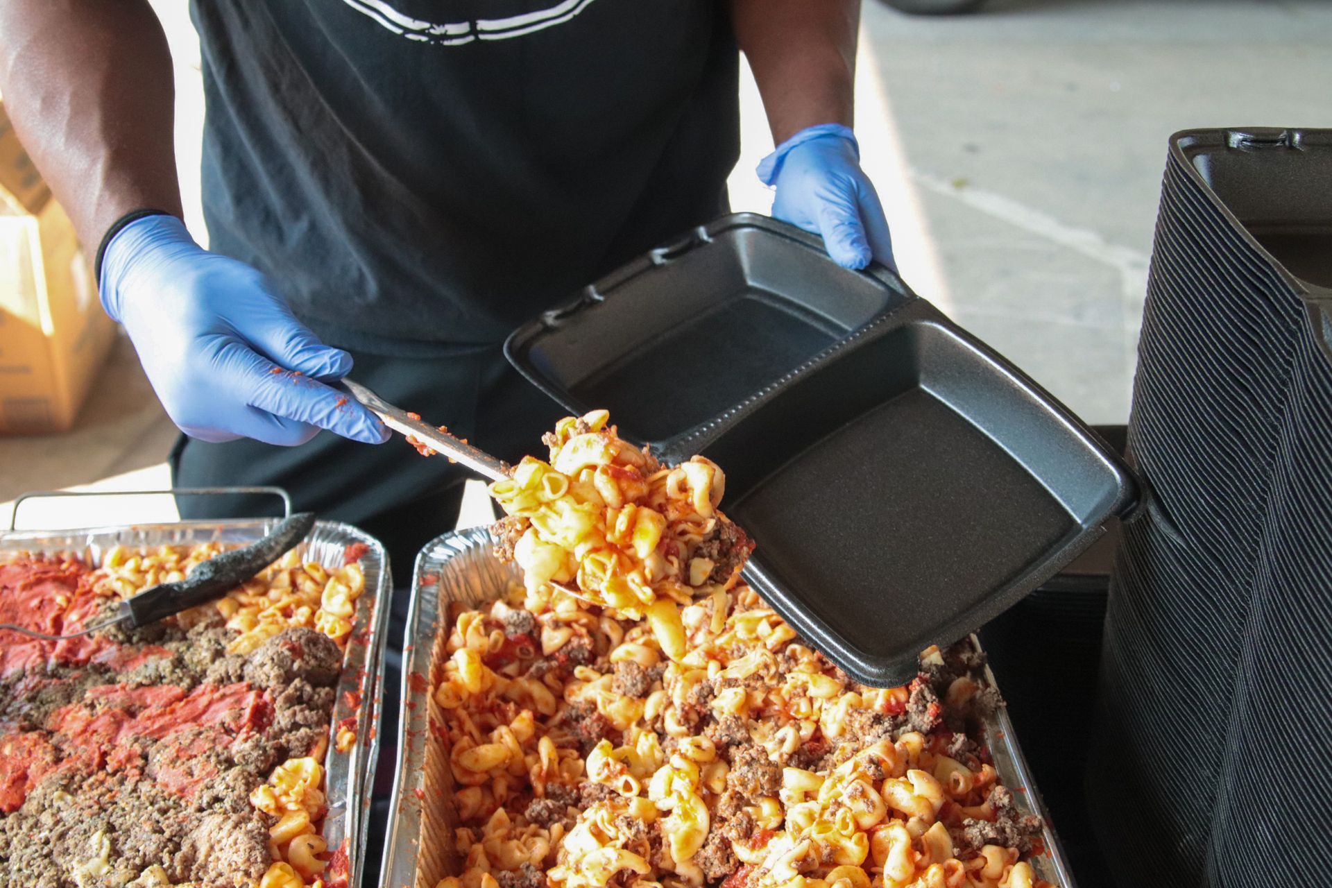 A man wearing blue gloves is holding a plastic tray of food.
