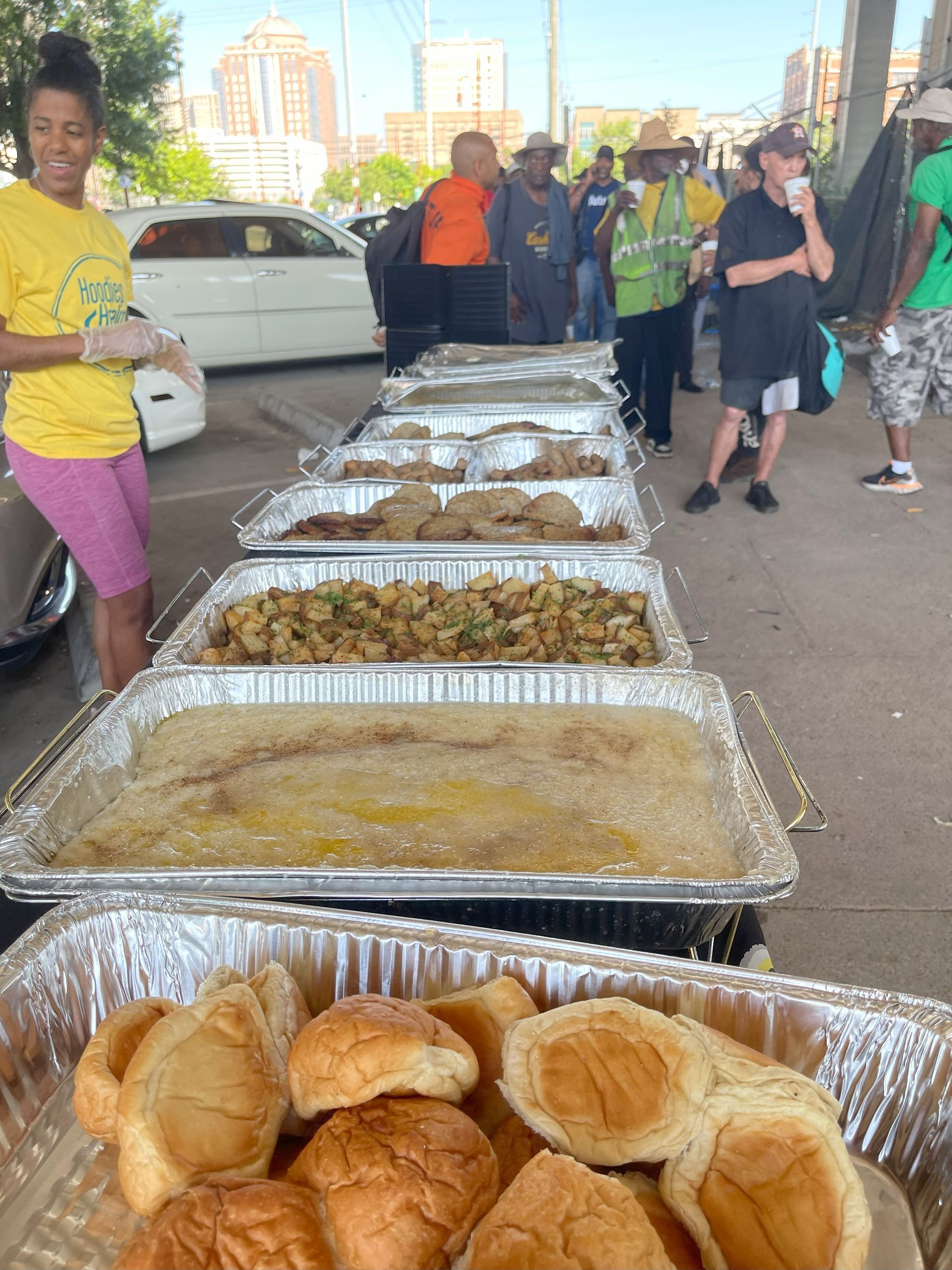A woman in a yellow shirt is standing next to a tray of food.