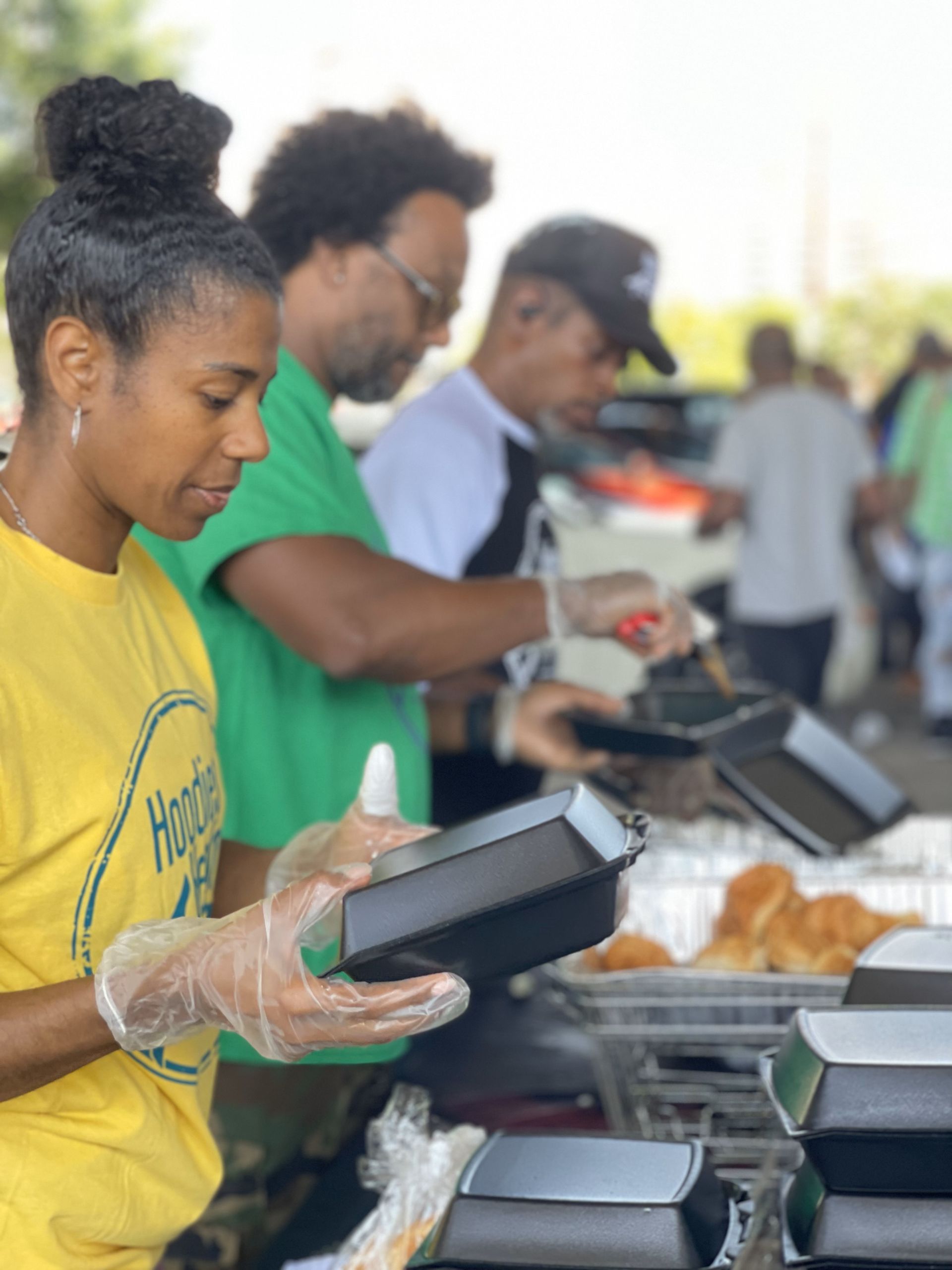 A woman in a yellow shirt is holding a box of food.
