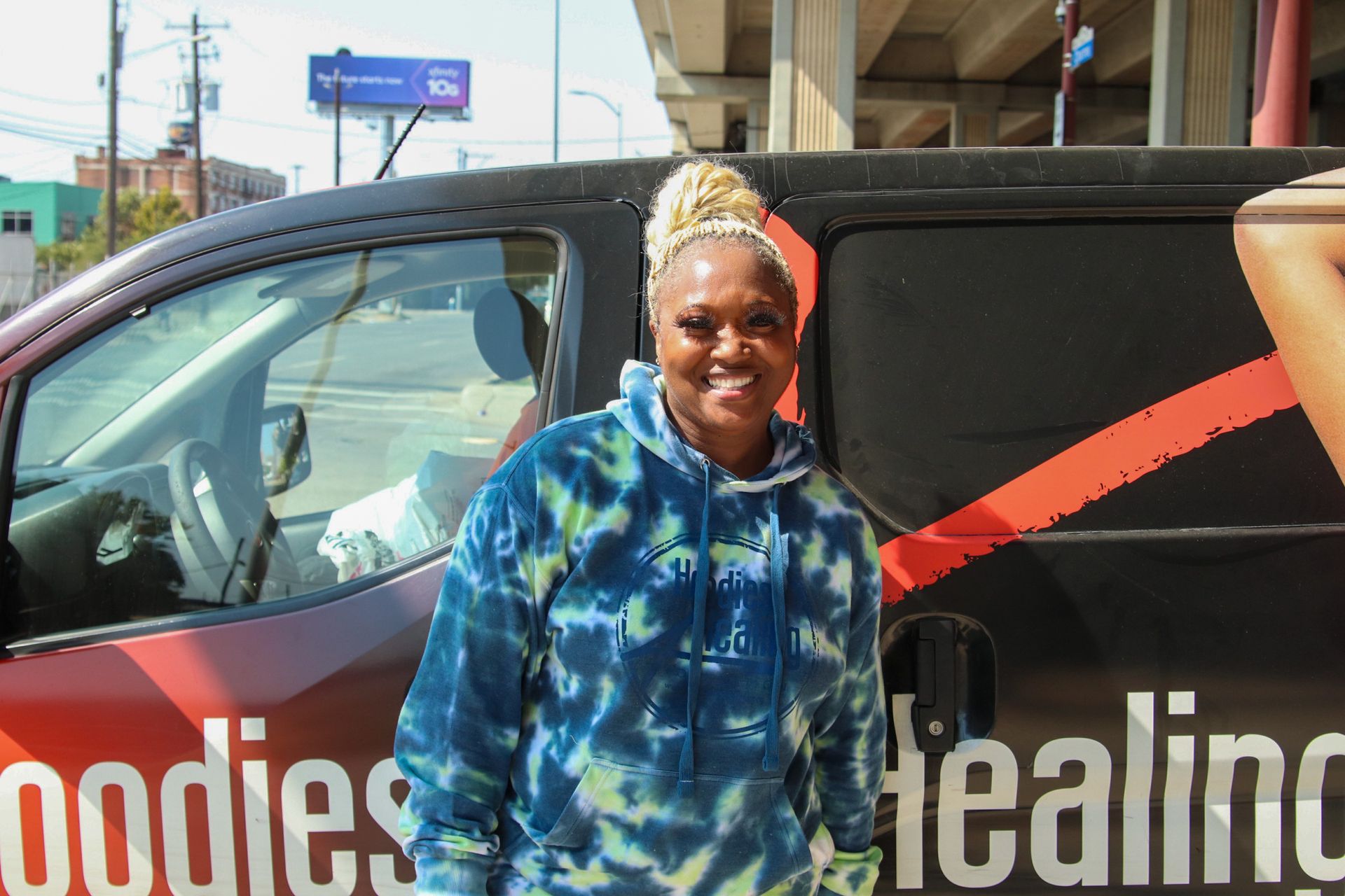 A woman is standing in front of a van that says bodies healing.