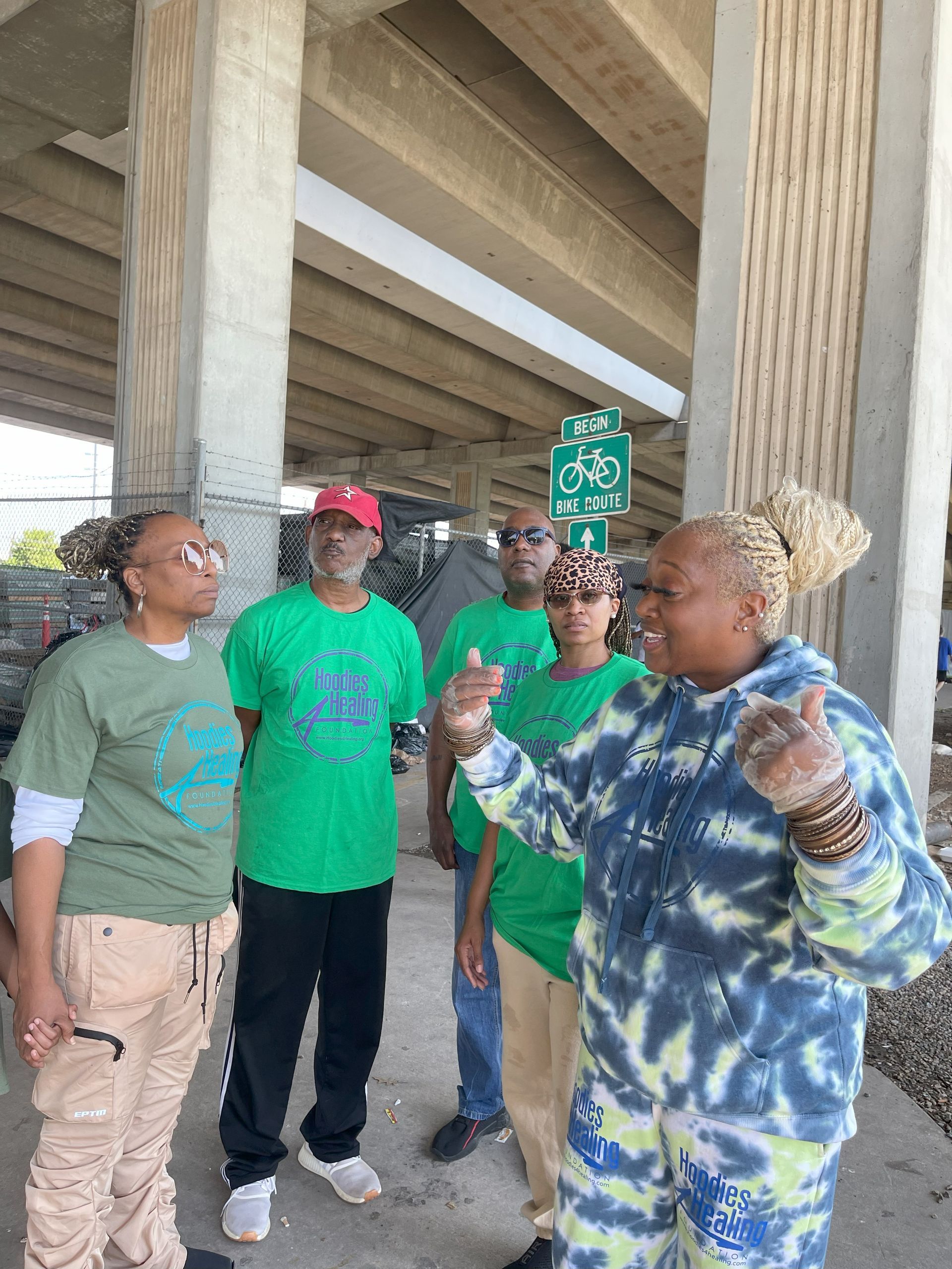 A group of people are standing under a bridge talking to each other.