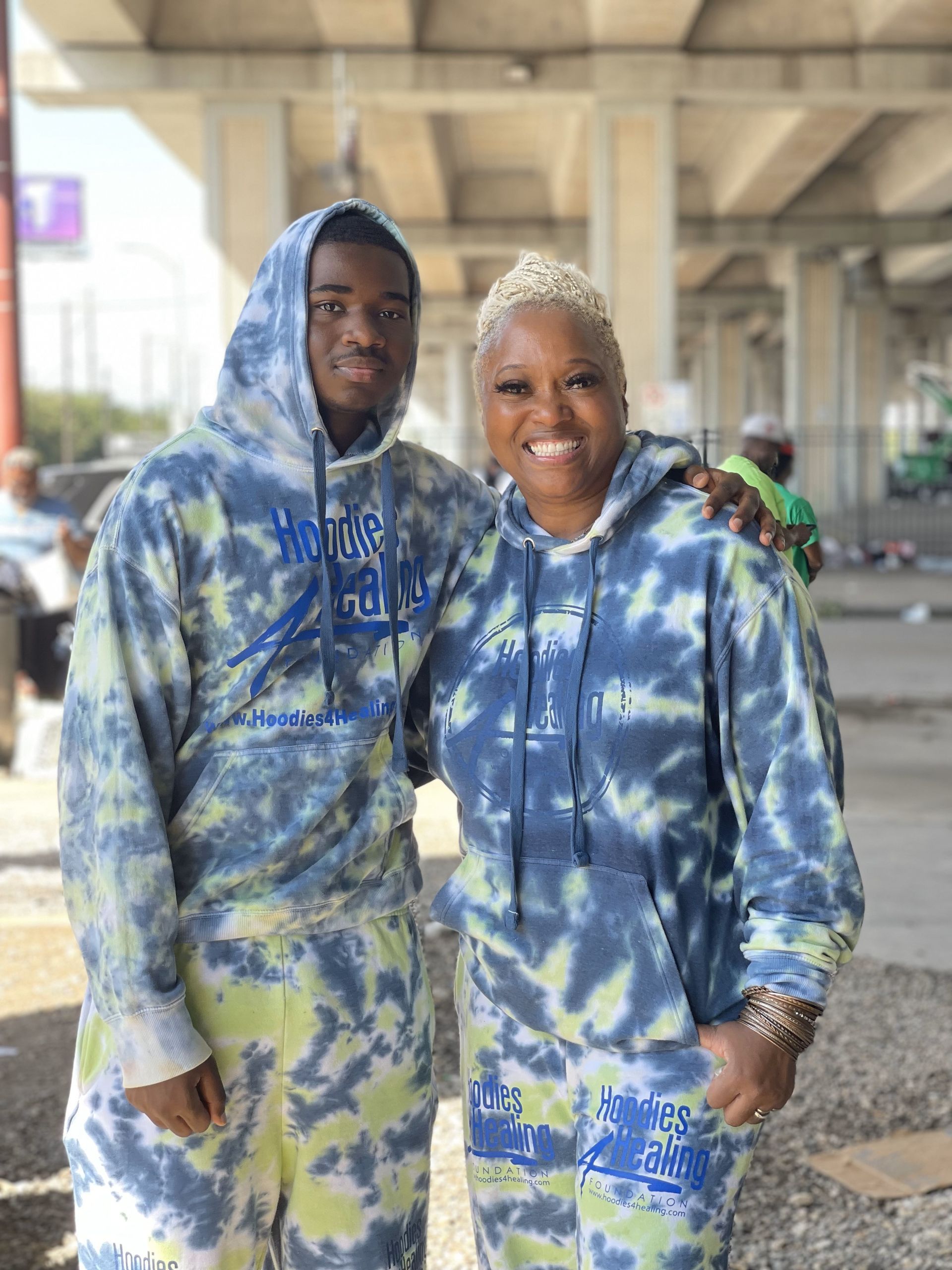 A man and a woman are standing next to each other wearing tie dye hoodies.