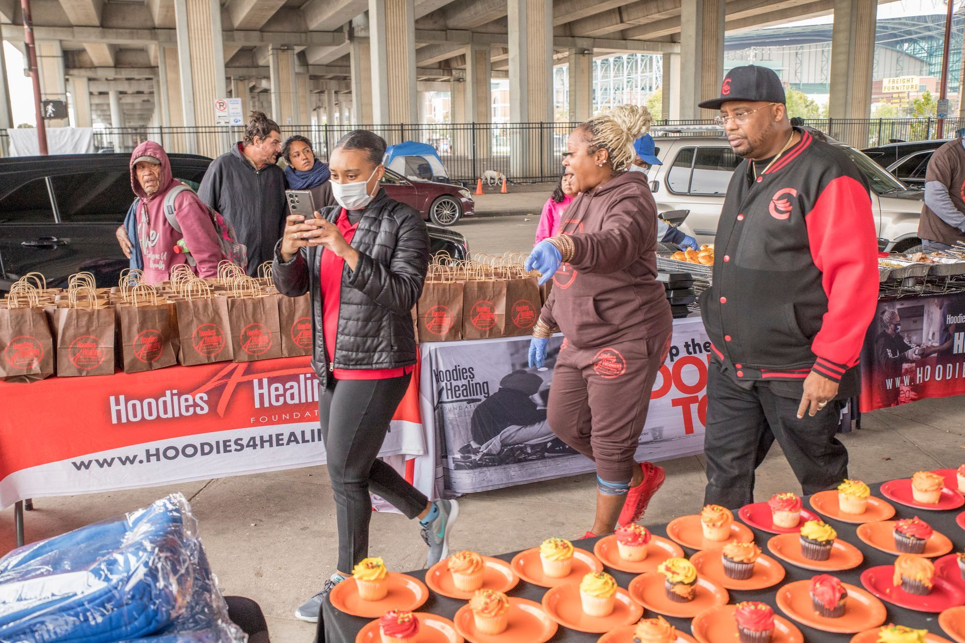 A group of people are standing around a table with cupcakes on it.